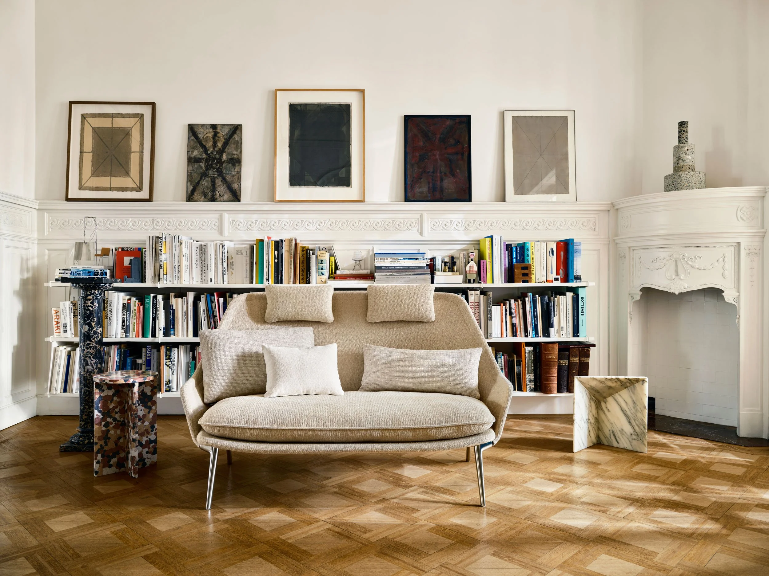 Home Stories for Winter 25 wurden beim Architekten David Van Severen und der Modefotografin Martina Bjorn fotografiert. Tiefes Bücherregal an Wand mit Bildern darüber. Slow Sofa in creme davor.