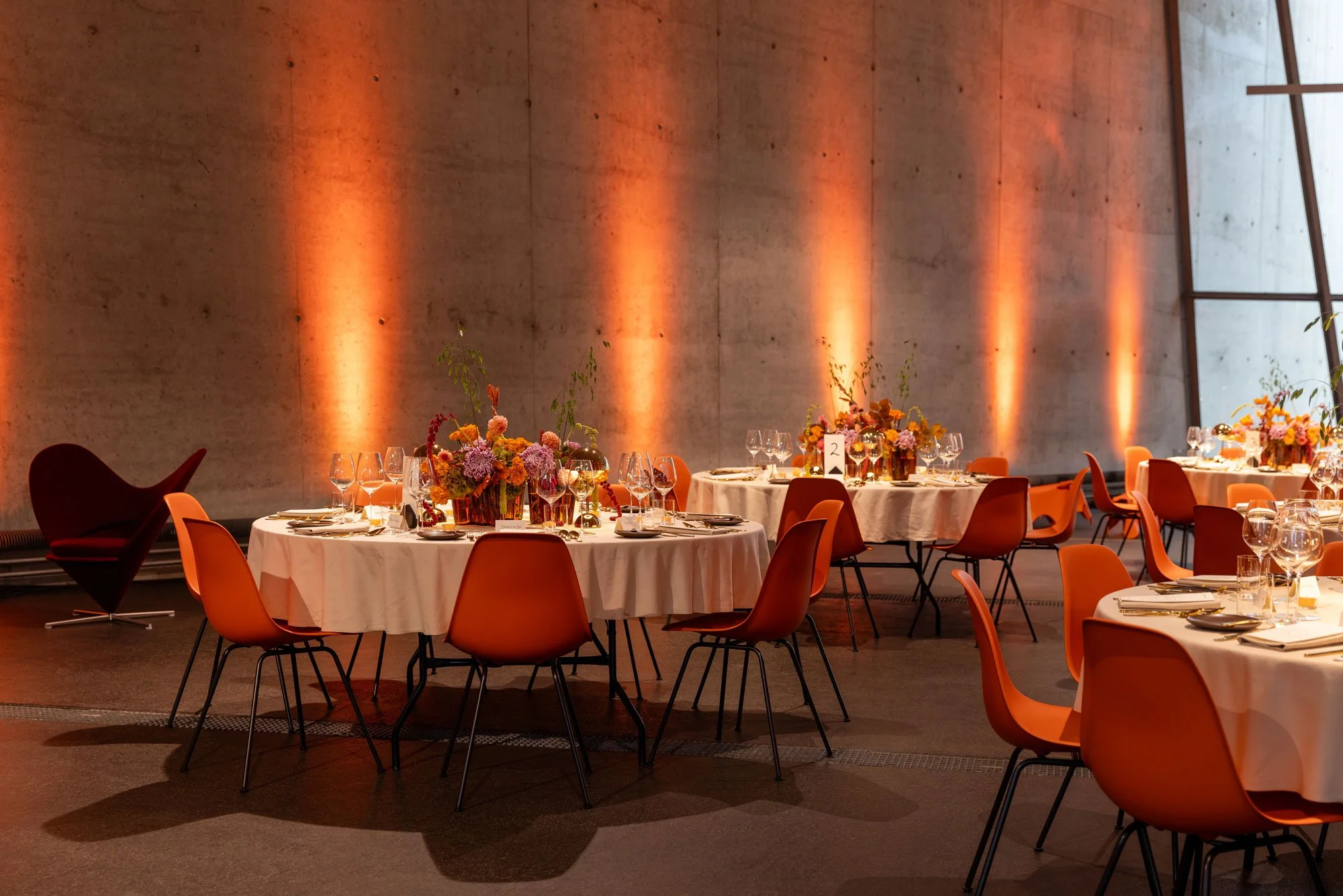 Das Gestaltungskonzept für das VIP-Dinner übersetzte die Farben und Formen des Doshi Retreats sowie die Atmosphäre des indischen Lichterfestes Diwali in eine europäische, zeitgemässe Ästhetik. orange Eames Plastic Stühle, farbige Blumen, oranges Lich