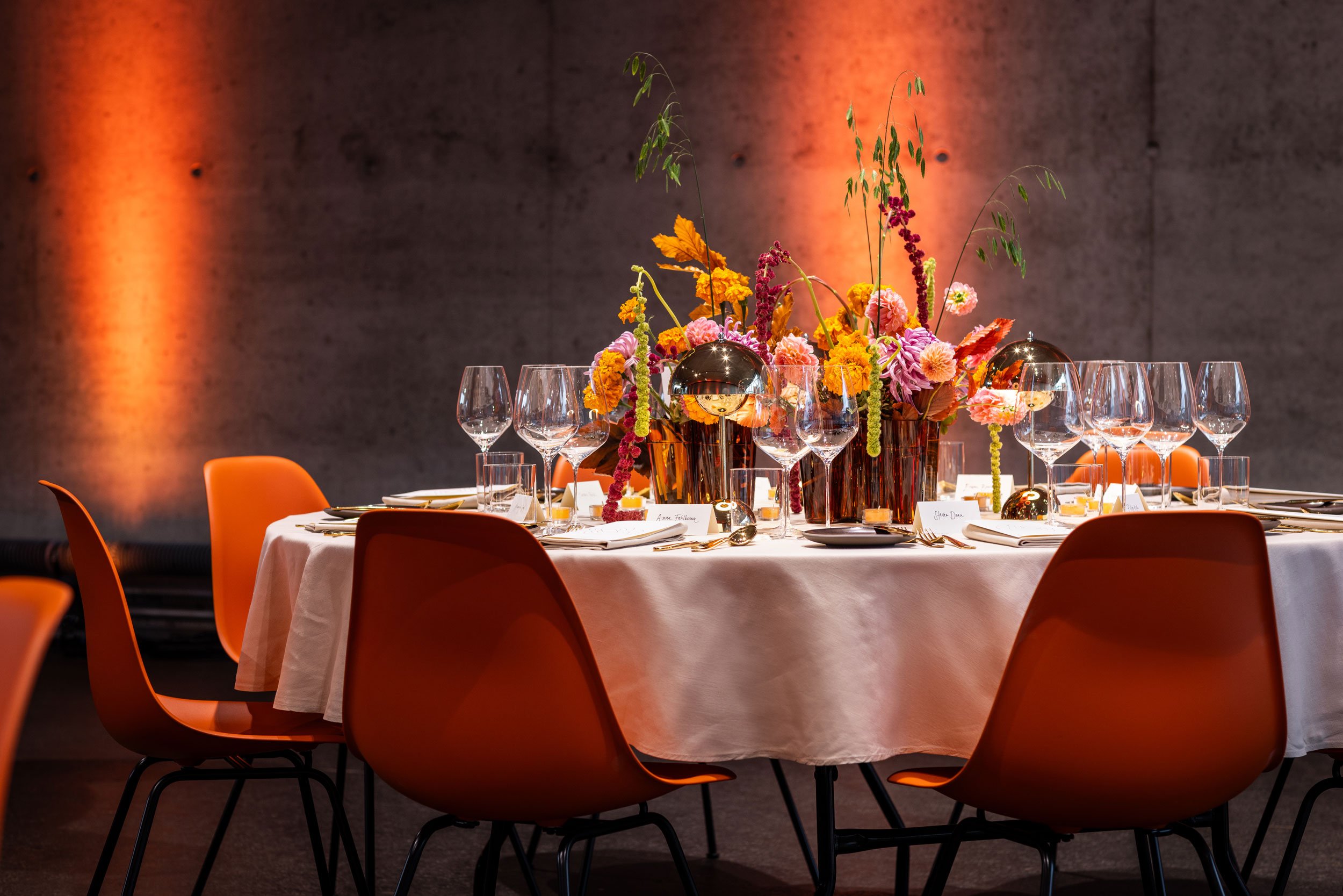 Das Gestaltungskonzept für das VIP-Dinner übersetzte die Farben und Formen des Doshi Retreats sowie die Atmosphäre des indischen Lichterfestes Diwali in eine europäische, zeitgemässe Ästhetik. orange Eames Plastic Stühle, farbige Blumen, oranges Lich