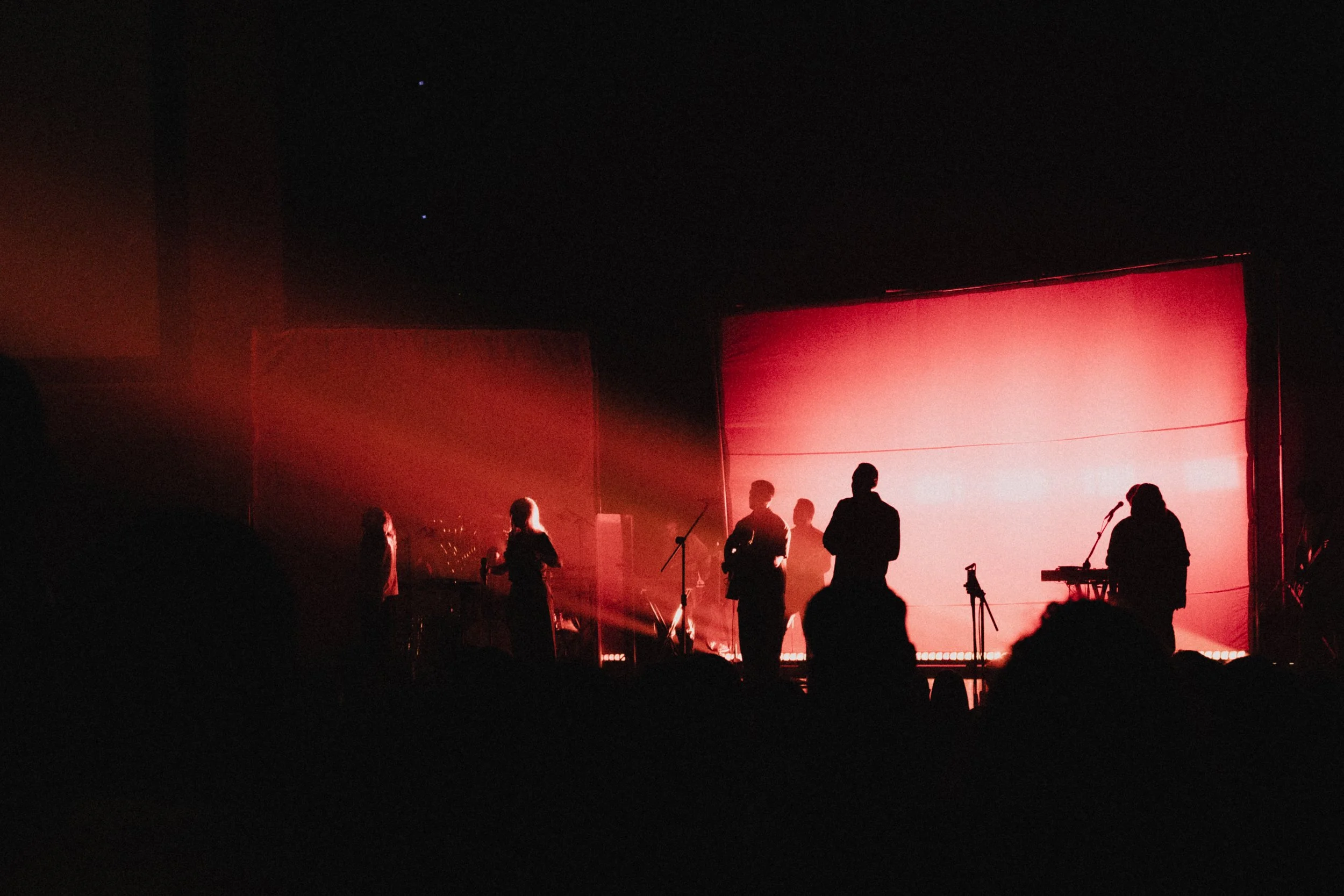 Silhouettes of musicians and a worship team on stage with a red backdrop and dramatic lighting.
