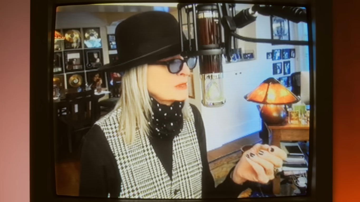 Diane Keaton singing into a microphone in a home setup for her "First Christmas" music video.