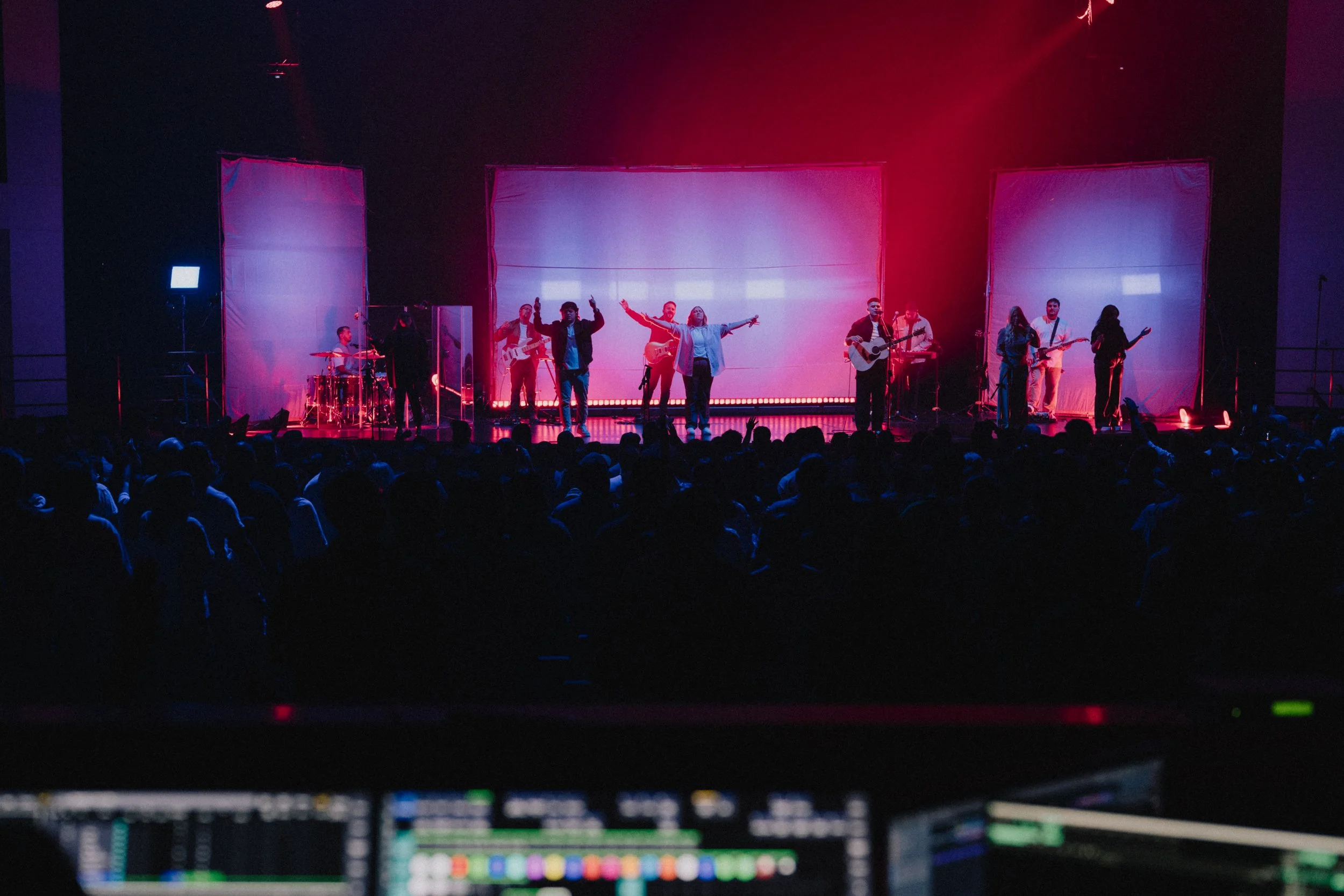 A large crowd watches a live worship album recording on stage, featuring musicians and singers with colourful lighting and technical equipment in the foreground. 