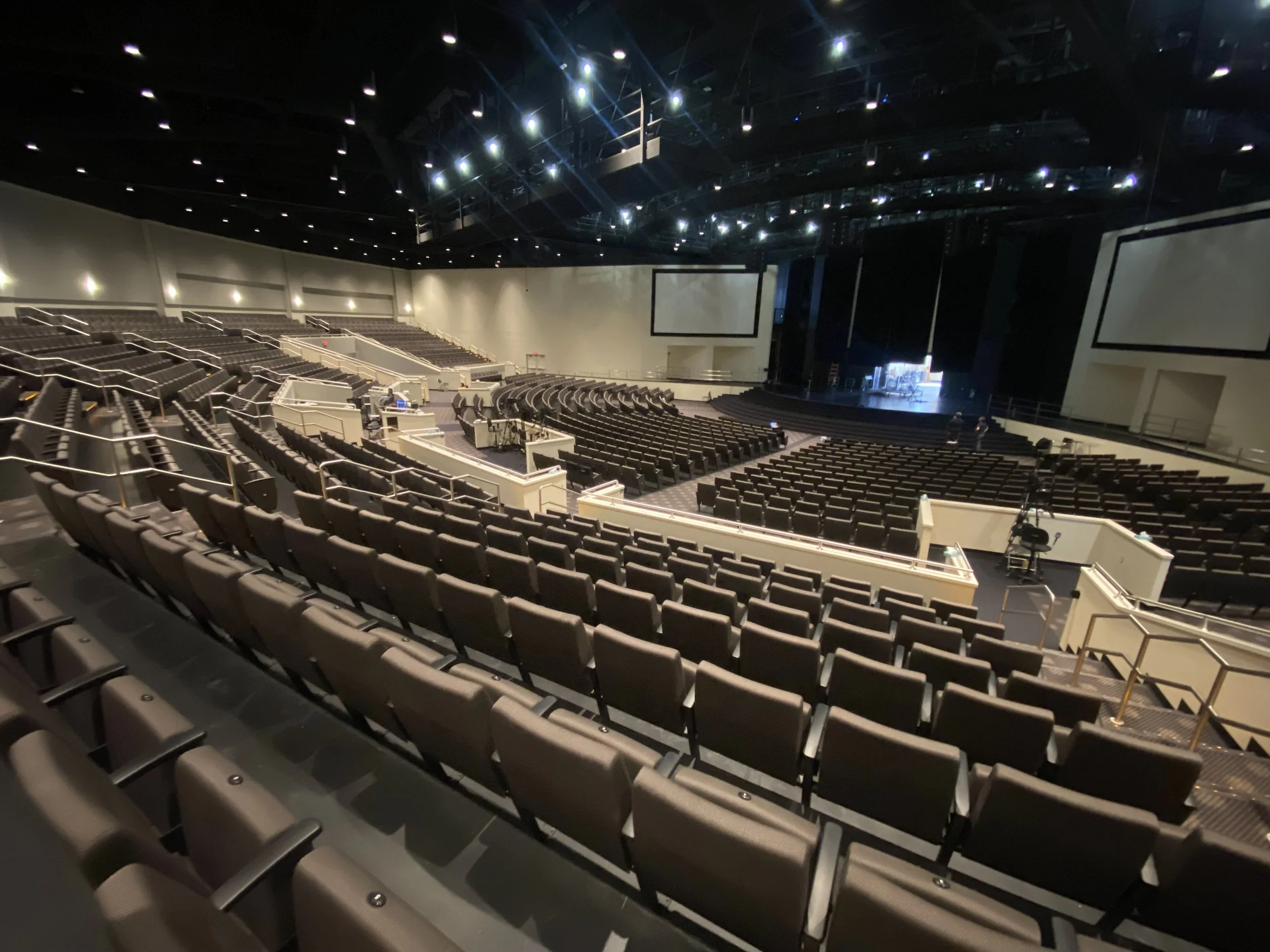 An empty auditorium with rows of brown seats and stage lights above, showcasing a performance stage at the front while a team sets up cameras and technical equipment.
