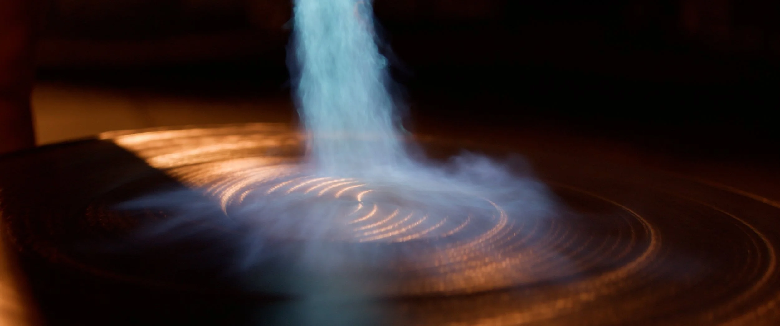 Close-up of a flame from a flame torch against the rippled surface of a metal plate during gong-making process.