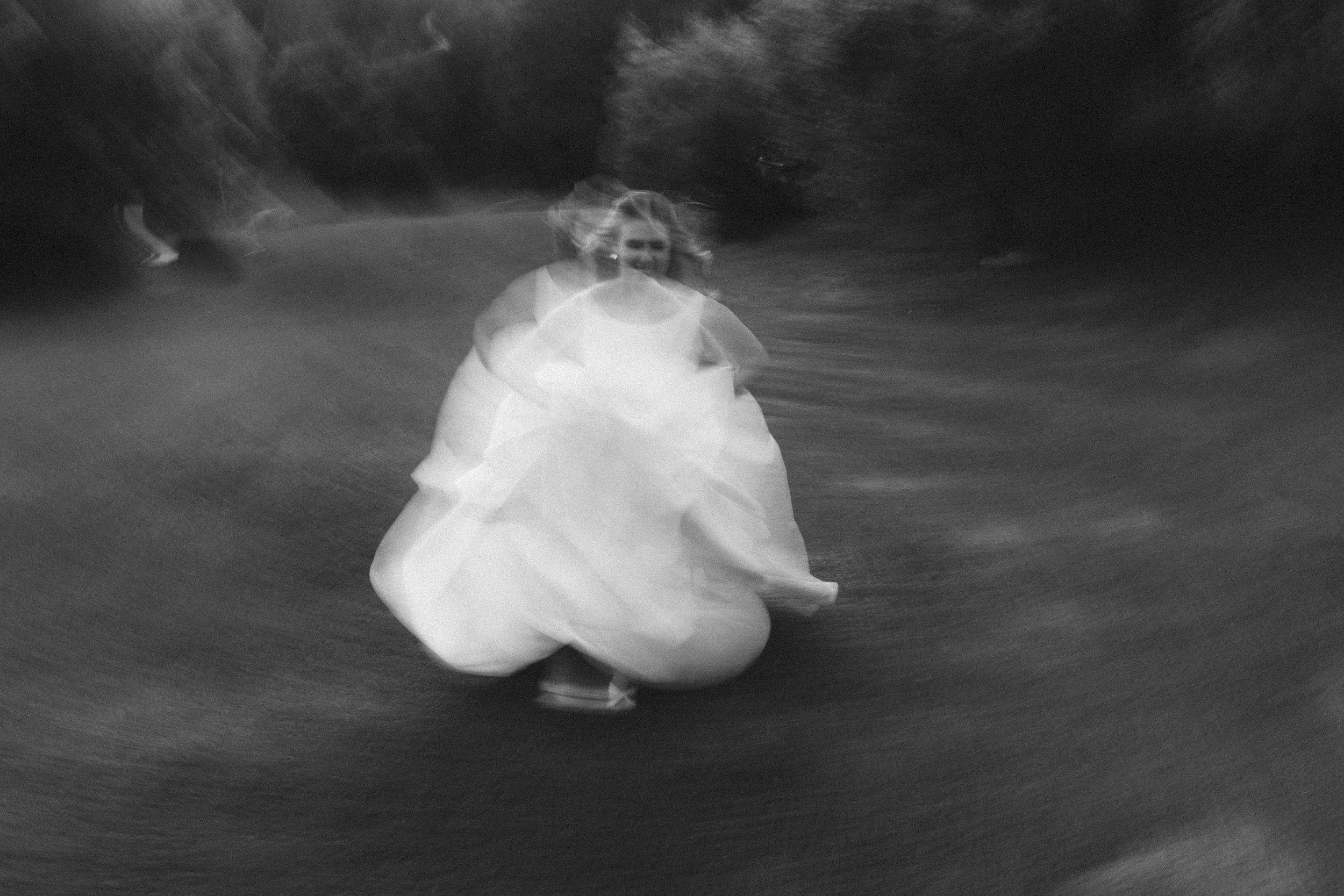 A blurred image captured on a film camera of a bride wearing a white wedding dress, running towards the camera on a grassy path.