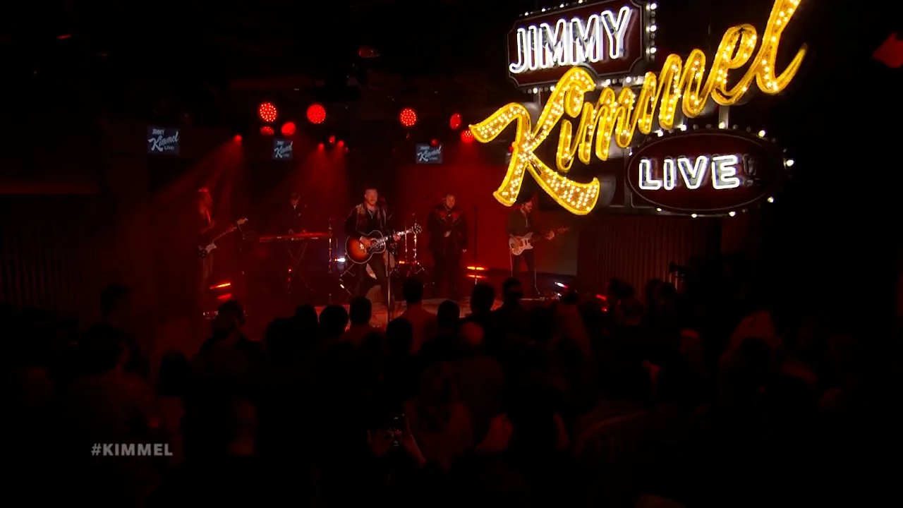 Live music performance at Jimmy Kimmel' Live! with Brandon Lake, Jelly Roll and band playing on stage and a live audience watching. Large illuminated sign displays 'Jimmy Kimmel Live'.