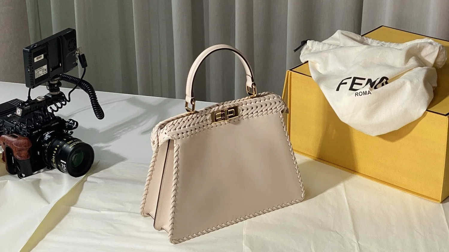 Close-up of professional video camera monitor showing fashion personality Bryan Yambao talking about the making of 'Fendi Roma: Peekaboo' bag at production facility with crafting tables in background.