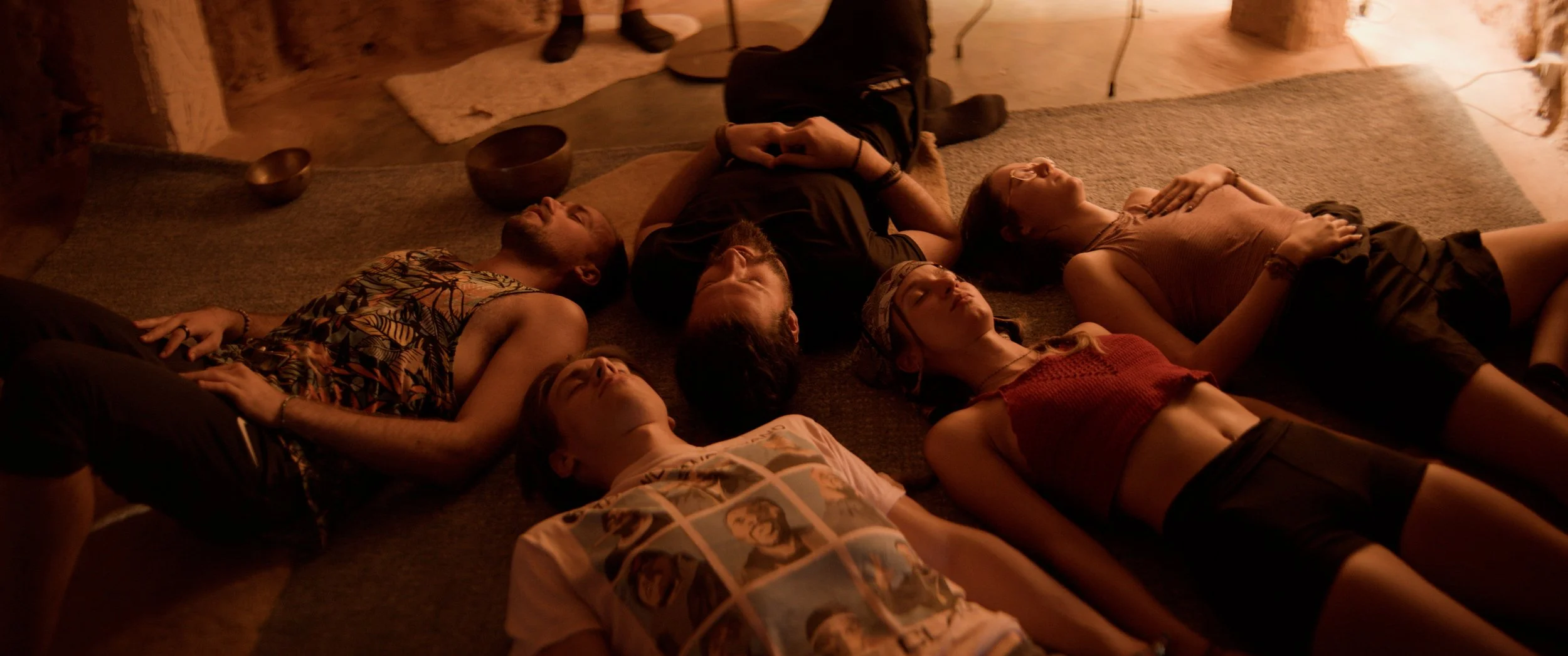 Group of people lying on the floor with eyes closed in a meditative state during the Gongmatic experience in a warm and dimly lit room.
