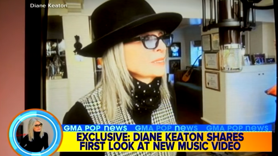 Screenshot of Good Morning America TV program titled, "Exclusive: Diane Keaton shares first look at new music video", featuring Diane wearing a black hat, glasses, and polka dot neck scarf in a home setting singing with a professional microphone.