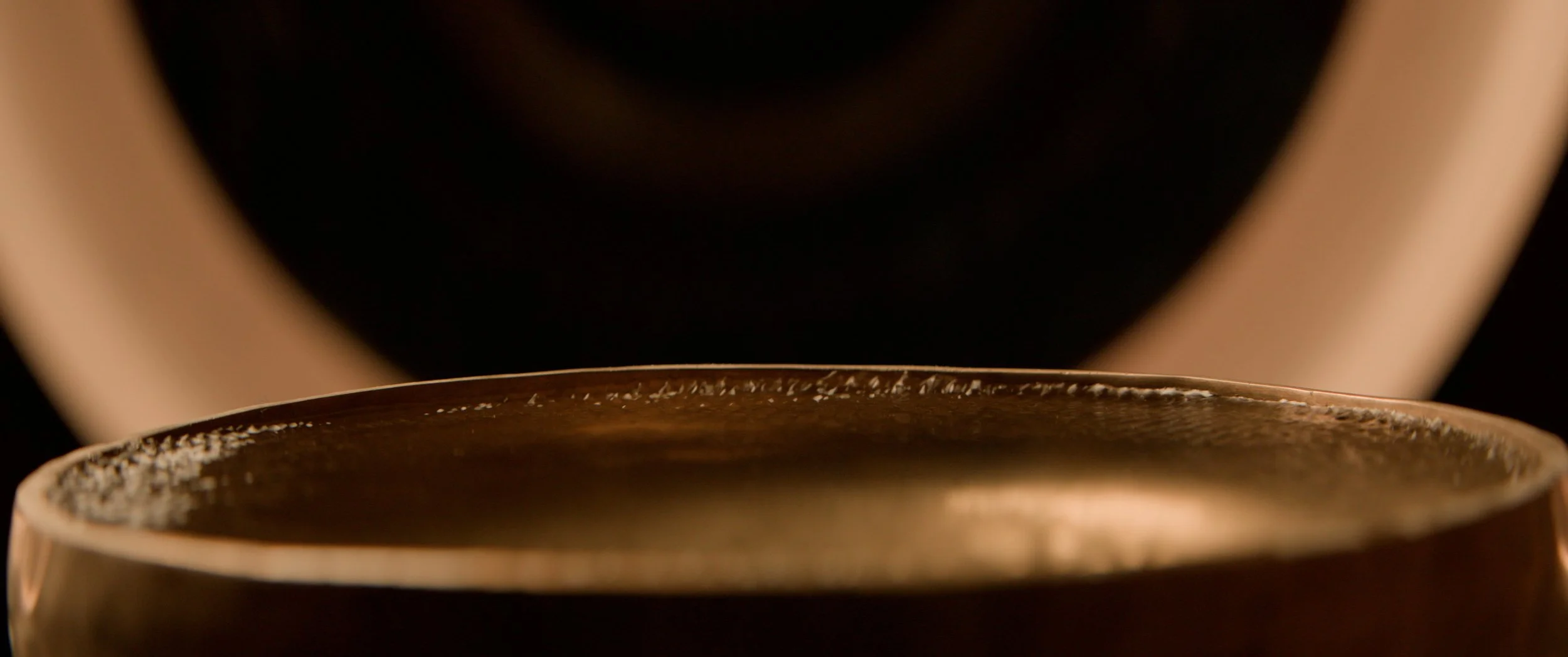 Close-up of soundwave ripple effect over water in a metal bowl with person standing in the background.