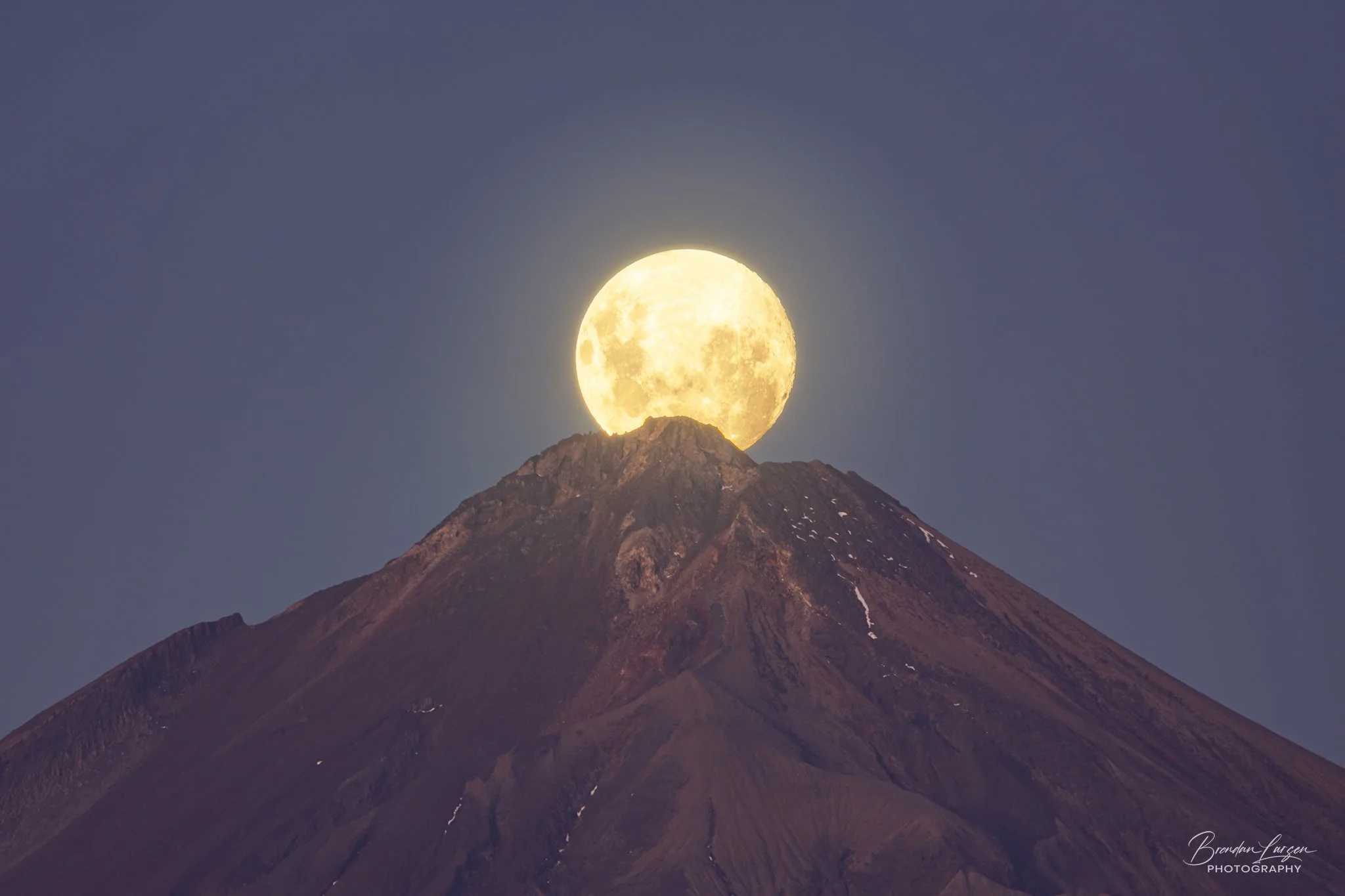Full moon rising behind a mountain with a clear evening sky.