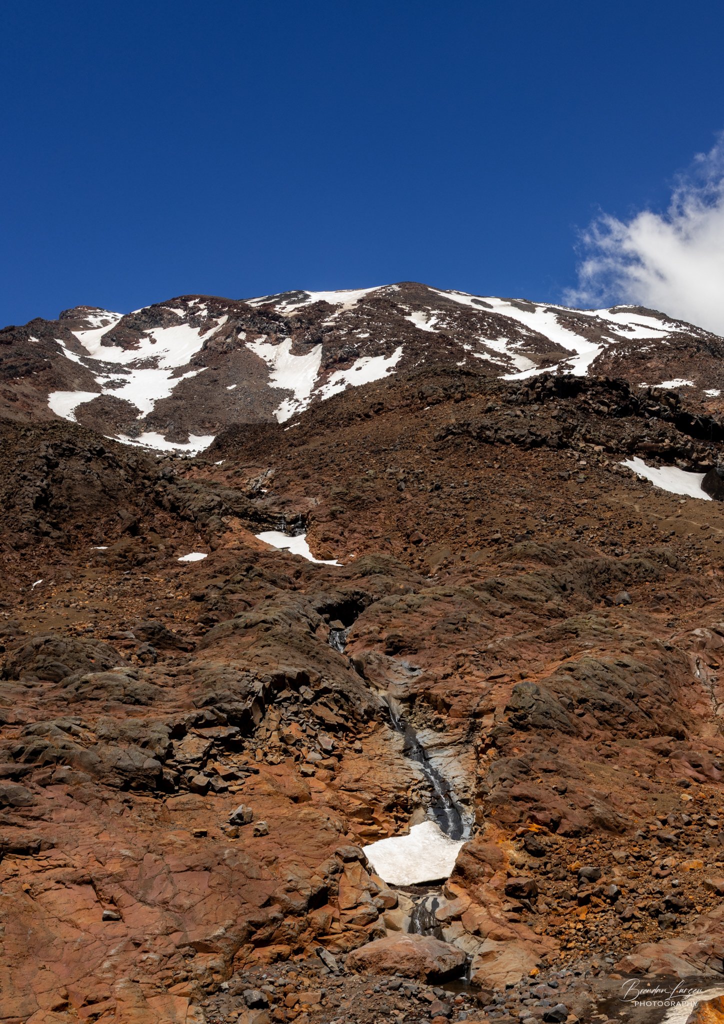 Mountain landscape with snow patches on rocky slopes and a blue sky.