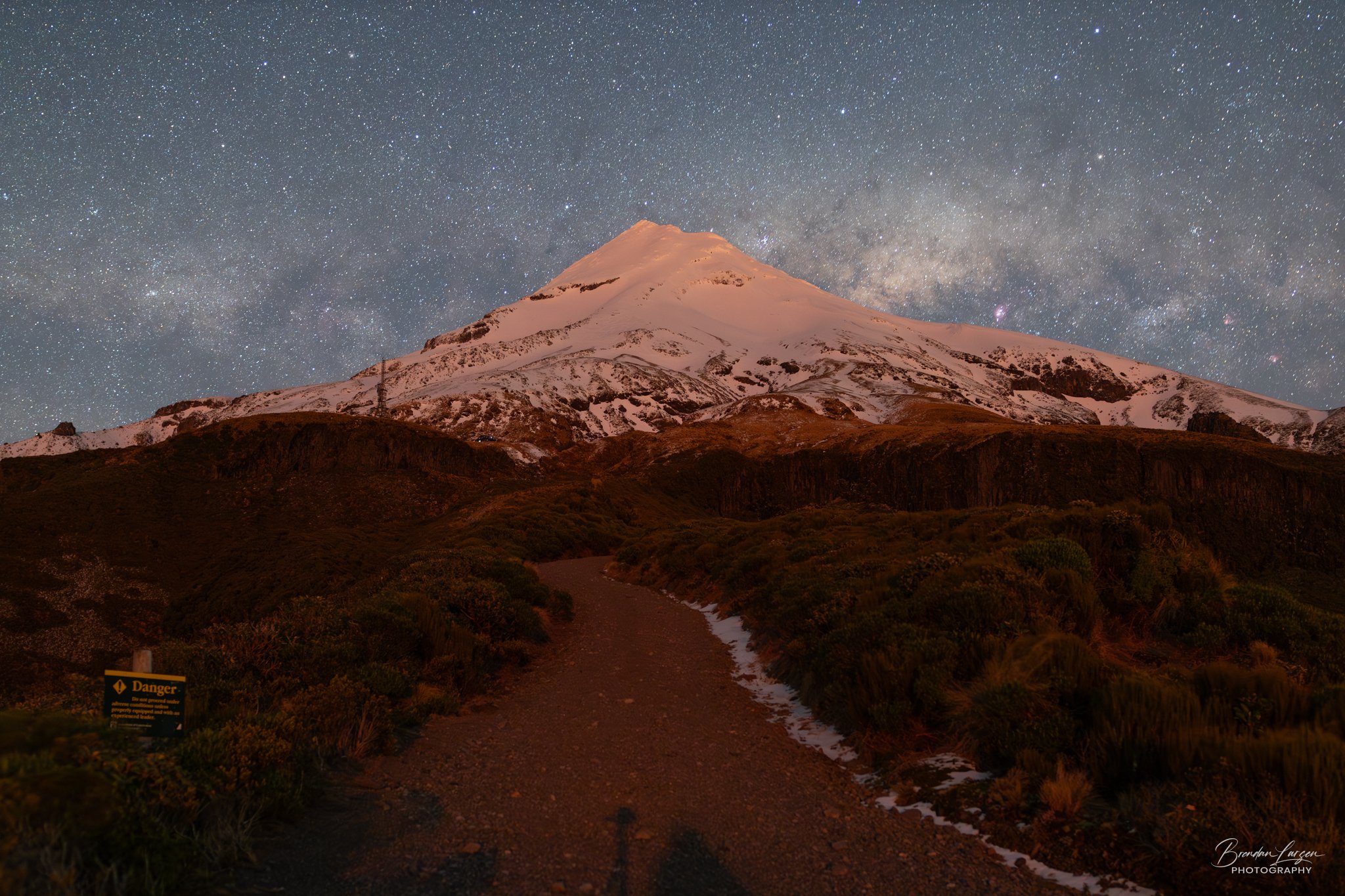 Nighttime view of snow-capped Mount Taranaki under a star-filled sky with the Milky Way galaxy visible.