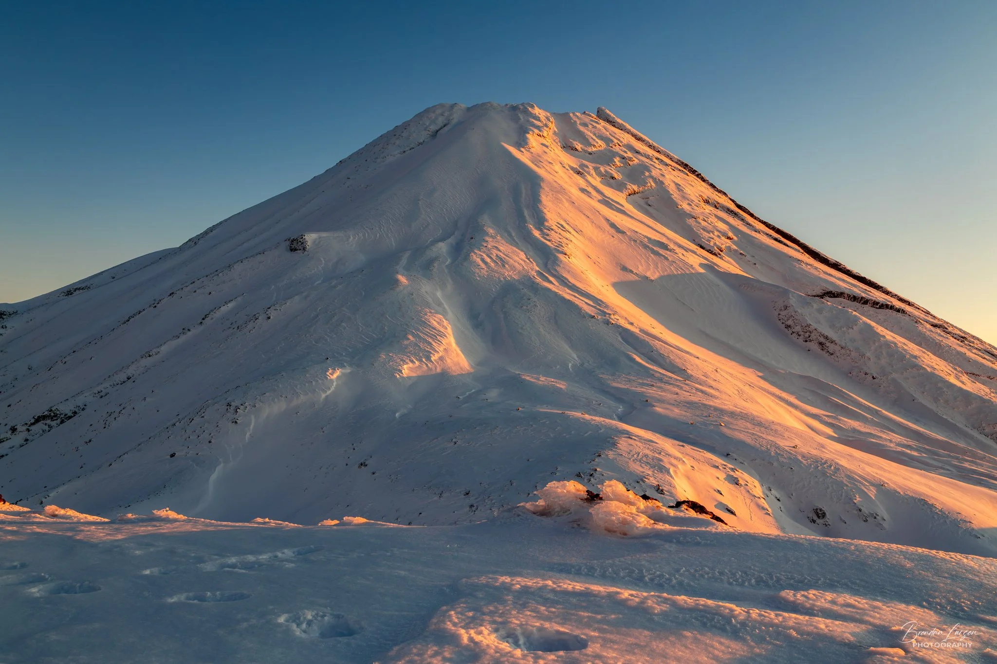 Snow-covered mountain peak during sunset with sunlight illuminating the snow and steep slopes.