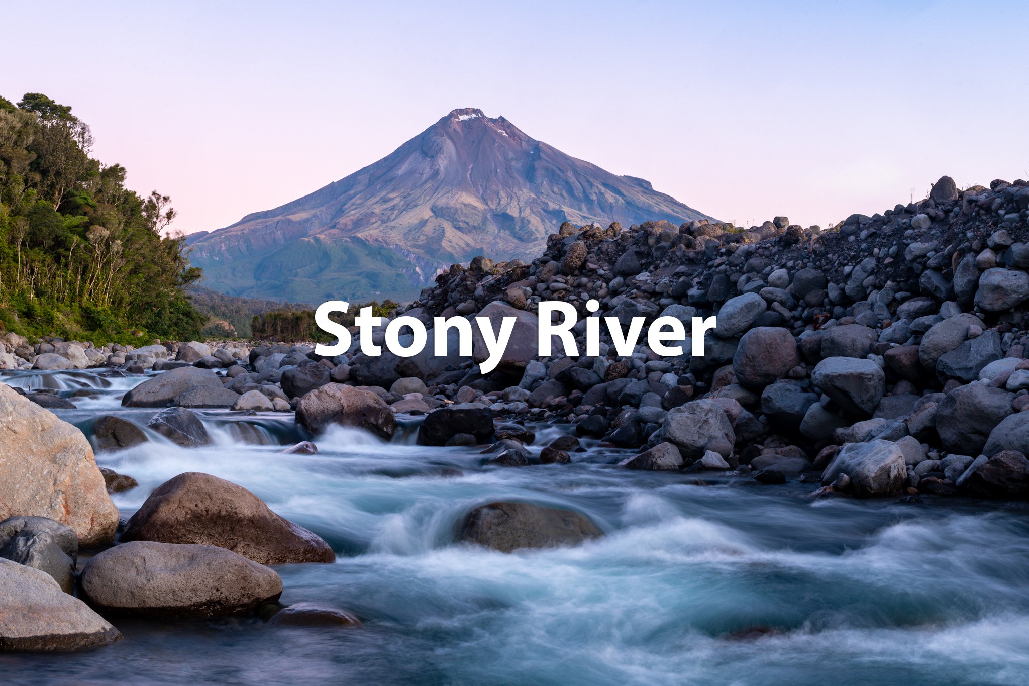 A river with rocks flowing through a landscape with a mountain in the background.