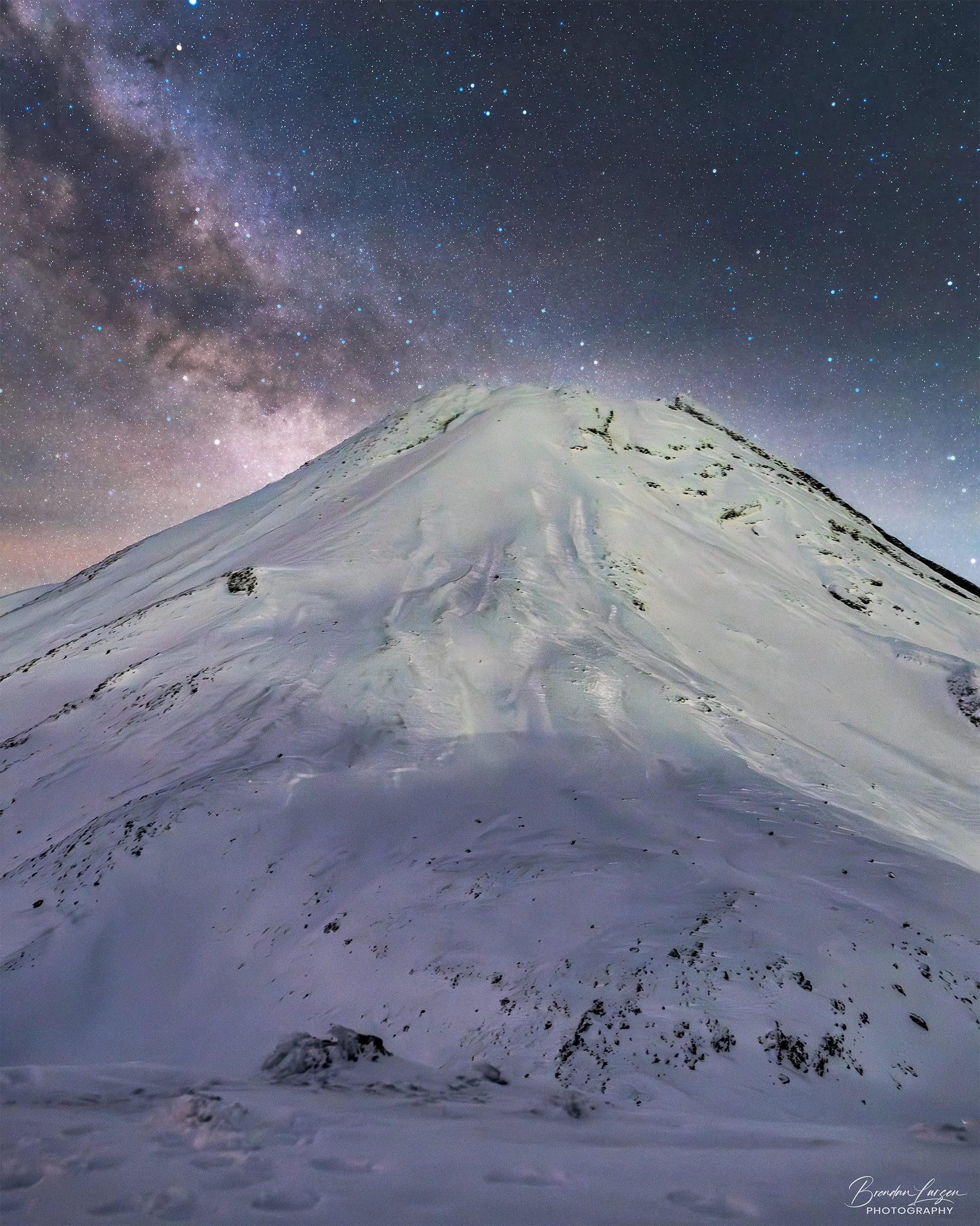 Snow-covered mountain under a starry night sky with the Milky Way galaxy visible.