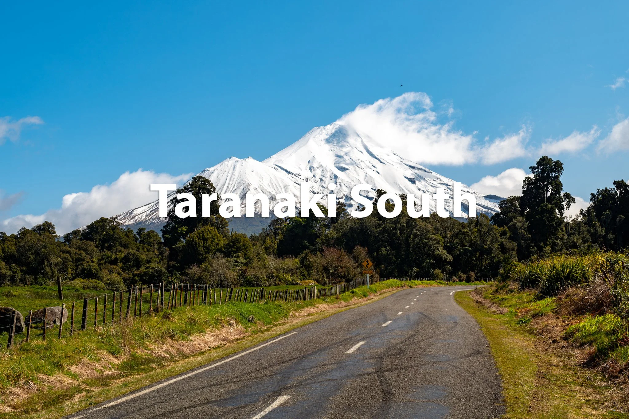 A winding country road with green grass on the sides, leading toward a snow-capped mountain in the background with the text 'Taranaki South' overlaid.