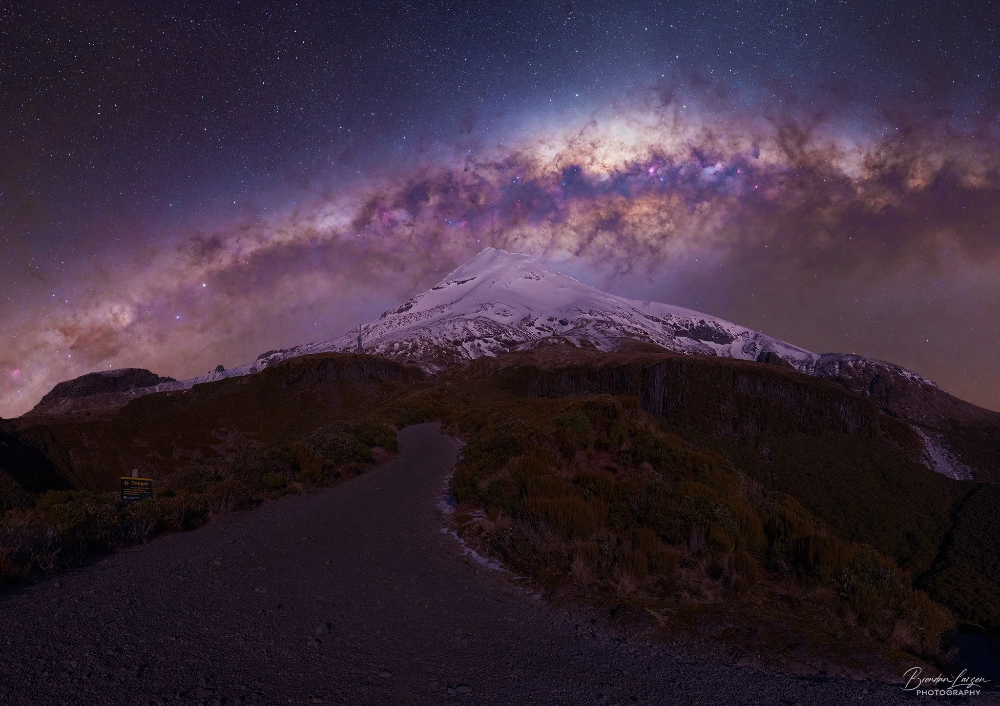 A snow-capped mountain under a starry night sky with the Milky Way galaxy prominently visible.