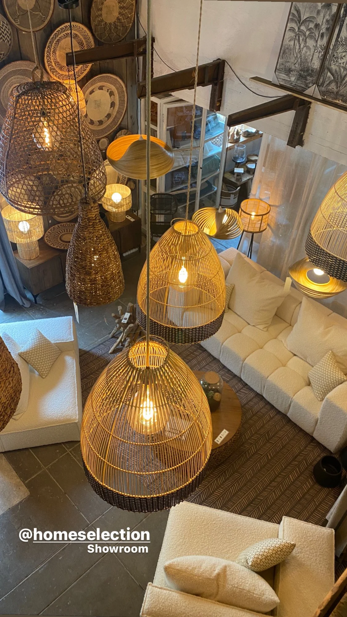 Intérieur d'un showroom avec des canapés blancs, des lampes suspendues en osier, et des objets décoratifs en osier sur les murs.