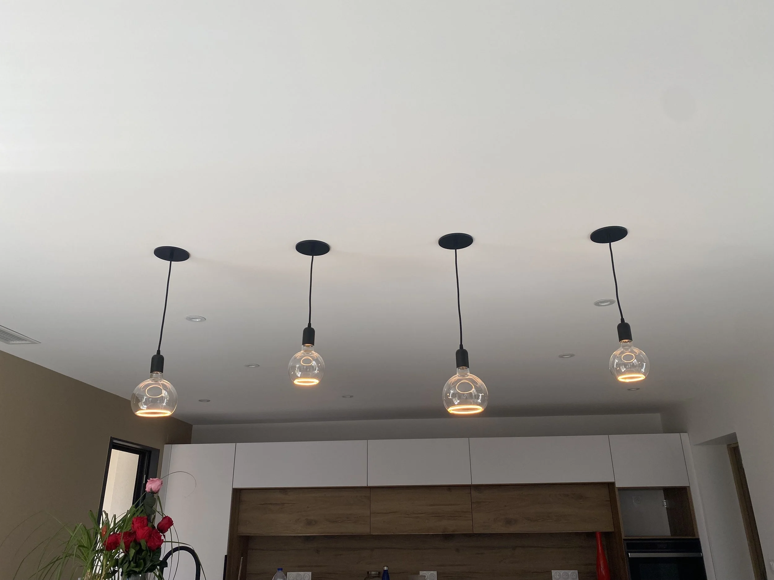 Cuisine moderne avec quatre suspensions lumineuses et un bouquet de fleurs sur le comptoir.