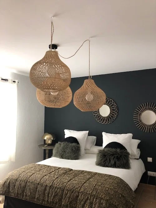 Chambre moderne avec lit double, oreillers décoratifs et luminaires en osier suspendus. Murs avec miroirs décoratifs et rideaux blancs.