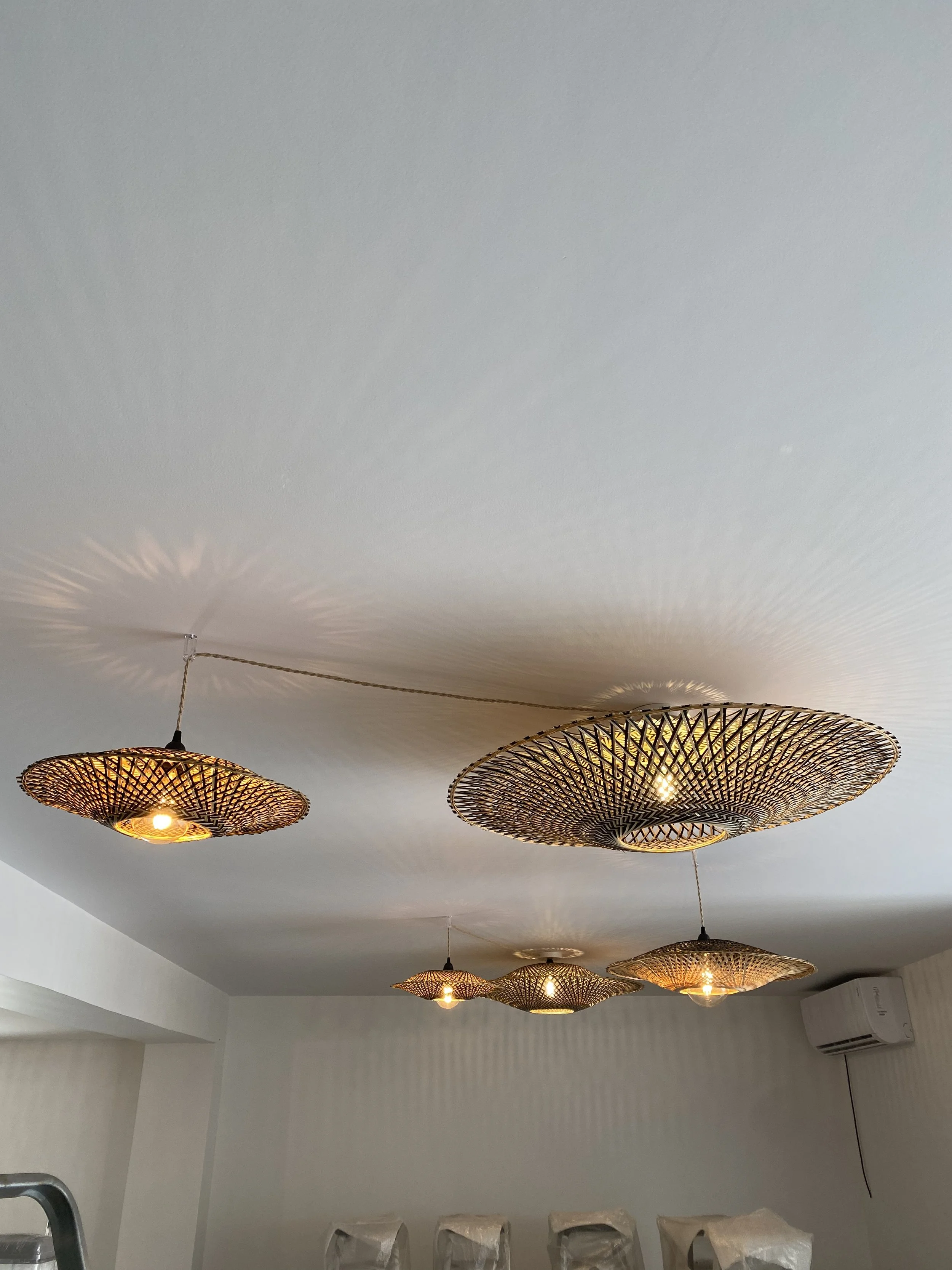 Suspensions lumineuses en rotin tressé au plafond d'une pièce, avec un climatiseur mural à droite.