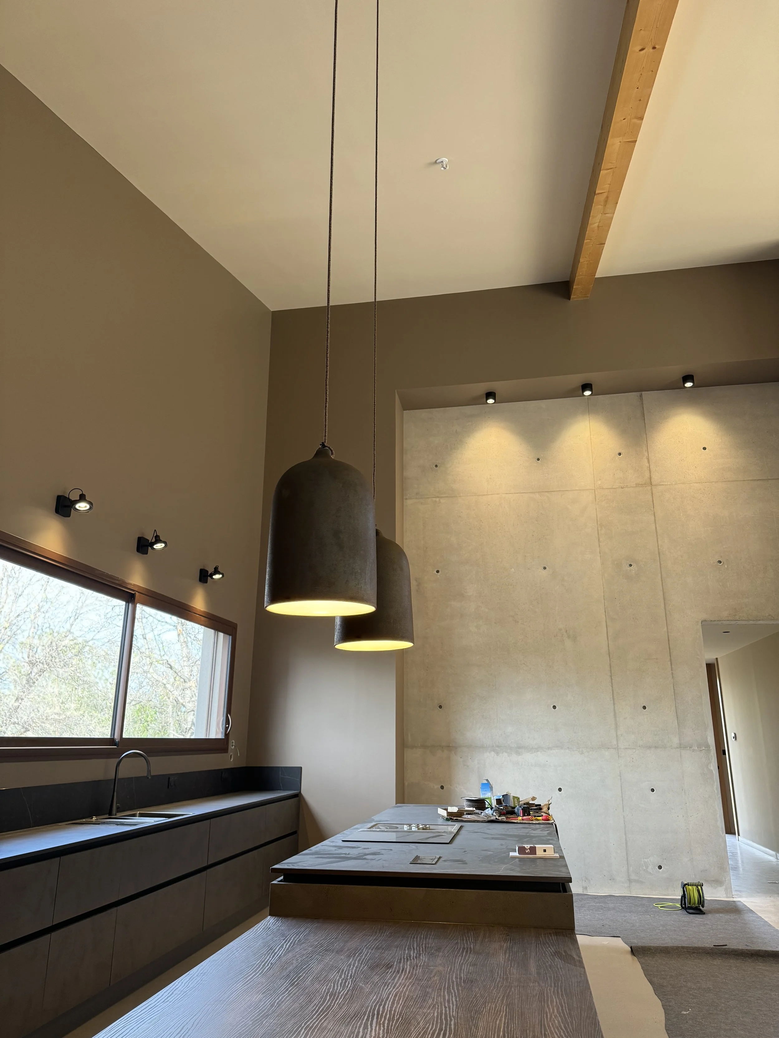 Cuisine moderne avec îlot central, suspensions céramique, murs en béton.