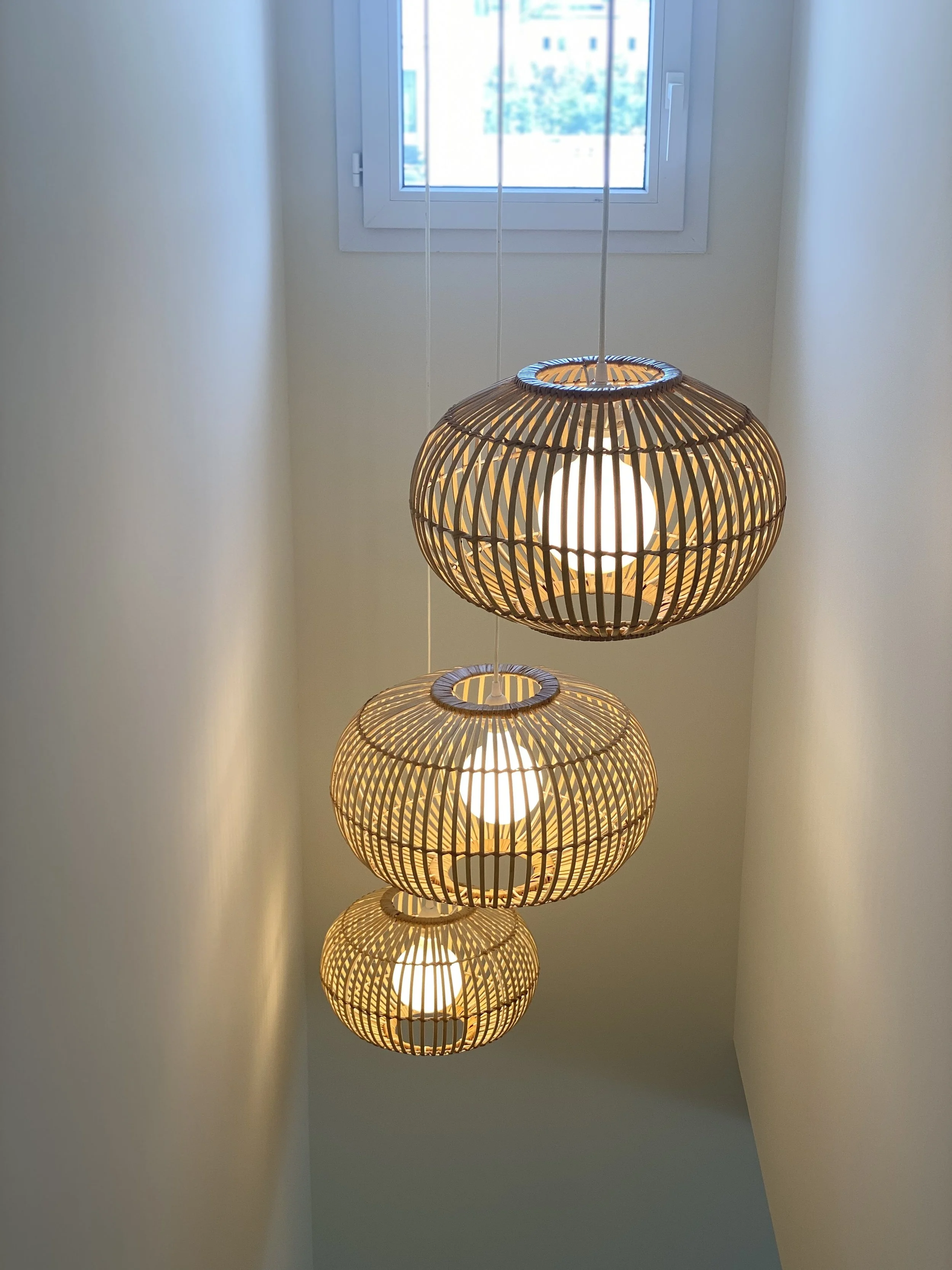 Trois suspensions en osier allumées dans un escalier sous une fenêtre lumineuse.