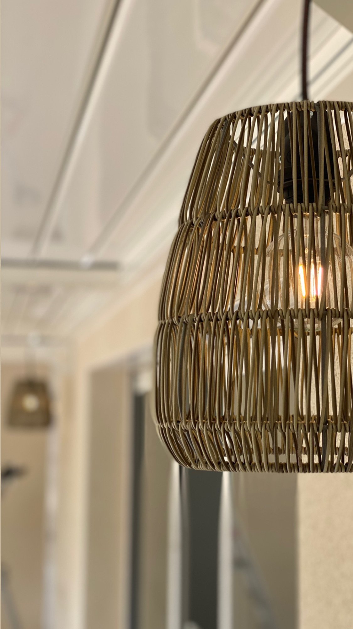 Suspension en osier avec ampoule allumée au plafond d'une pièce moderne.