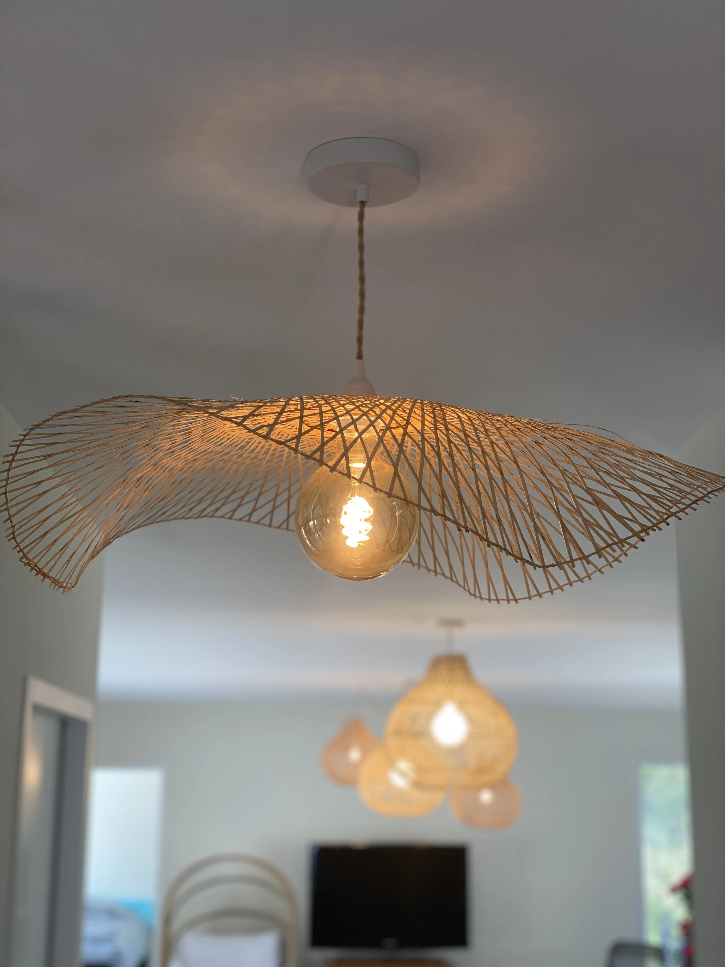 Suspension en osier avec ampoule allumée dans une pièce moderne.