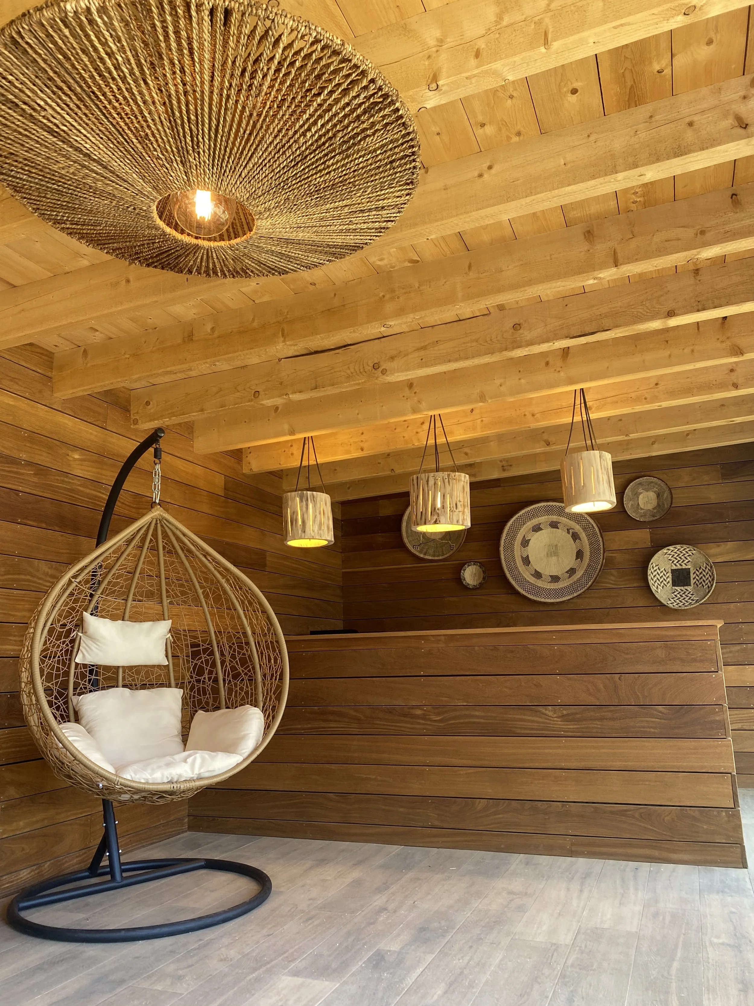 Intérieur en bois avec un fauteuil suspendu, lampes suspendues, et décorations murales rondes.
