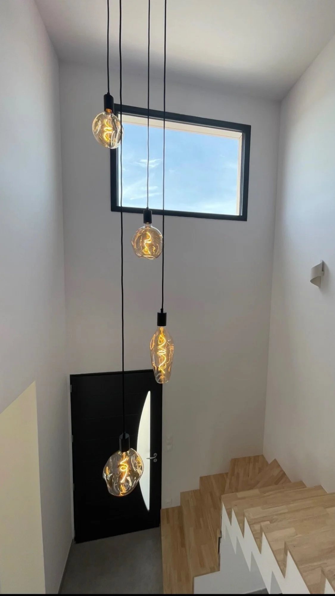 Escalier intérieur moderne avec lampes suspendues et fenêtre rectangulaire.