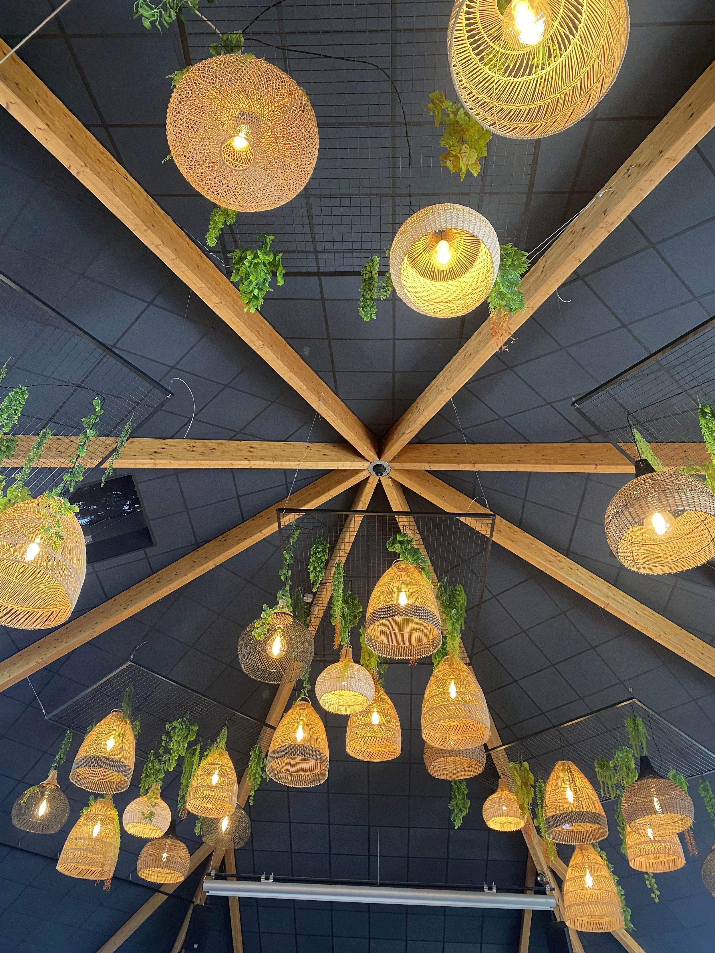 Plafond avec des luminaires suspendus en osier et des plantes vertes artificielles.