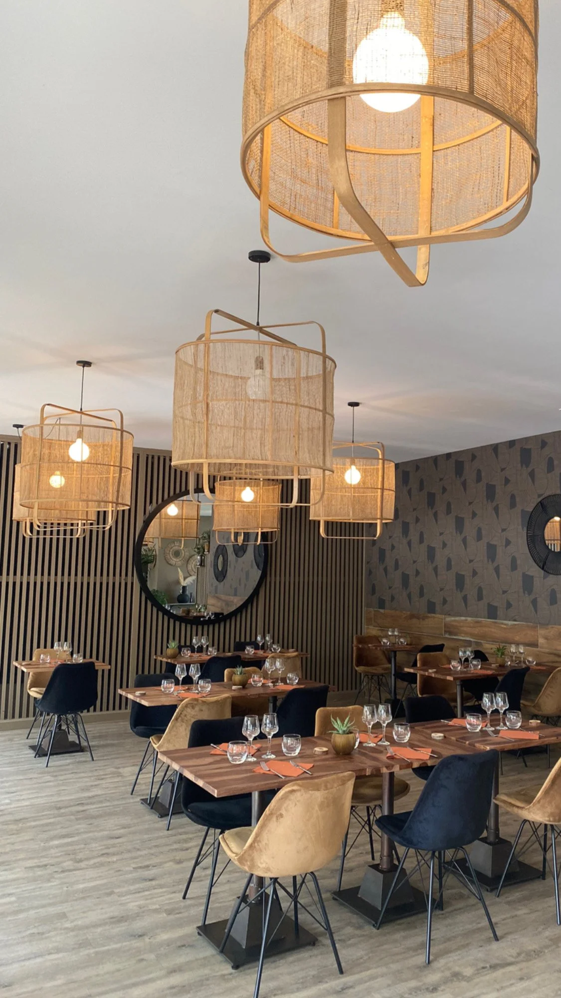 Intérieur d'un restaurant moderne avec des tables et chaises élégantes, des luminaires suspendus et une décoration murale raffinée.