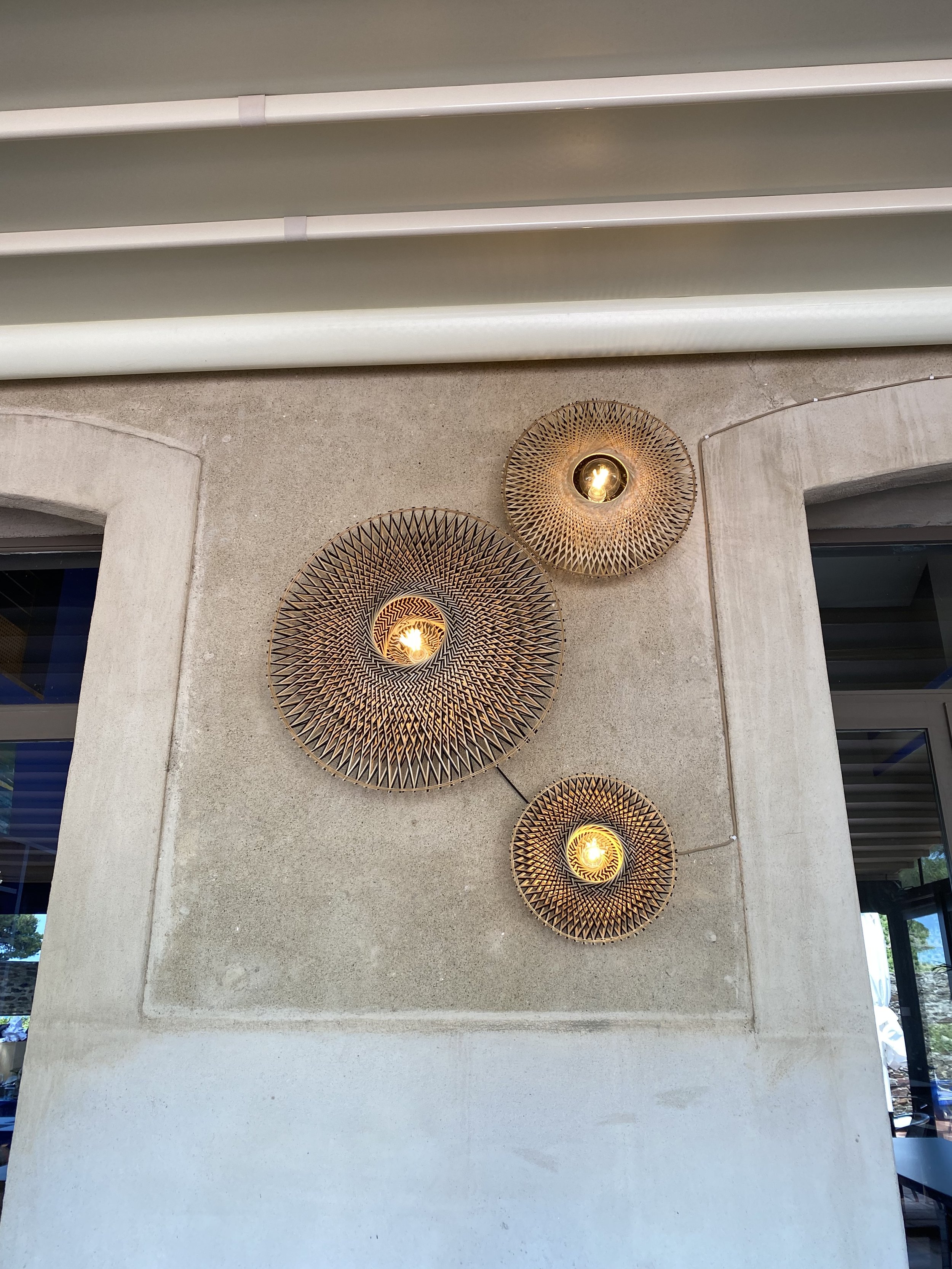 Trois appliques murales circulaires en rotin décorent un mur beige sous un plafond à lamelles blanches.