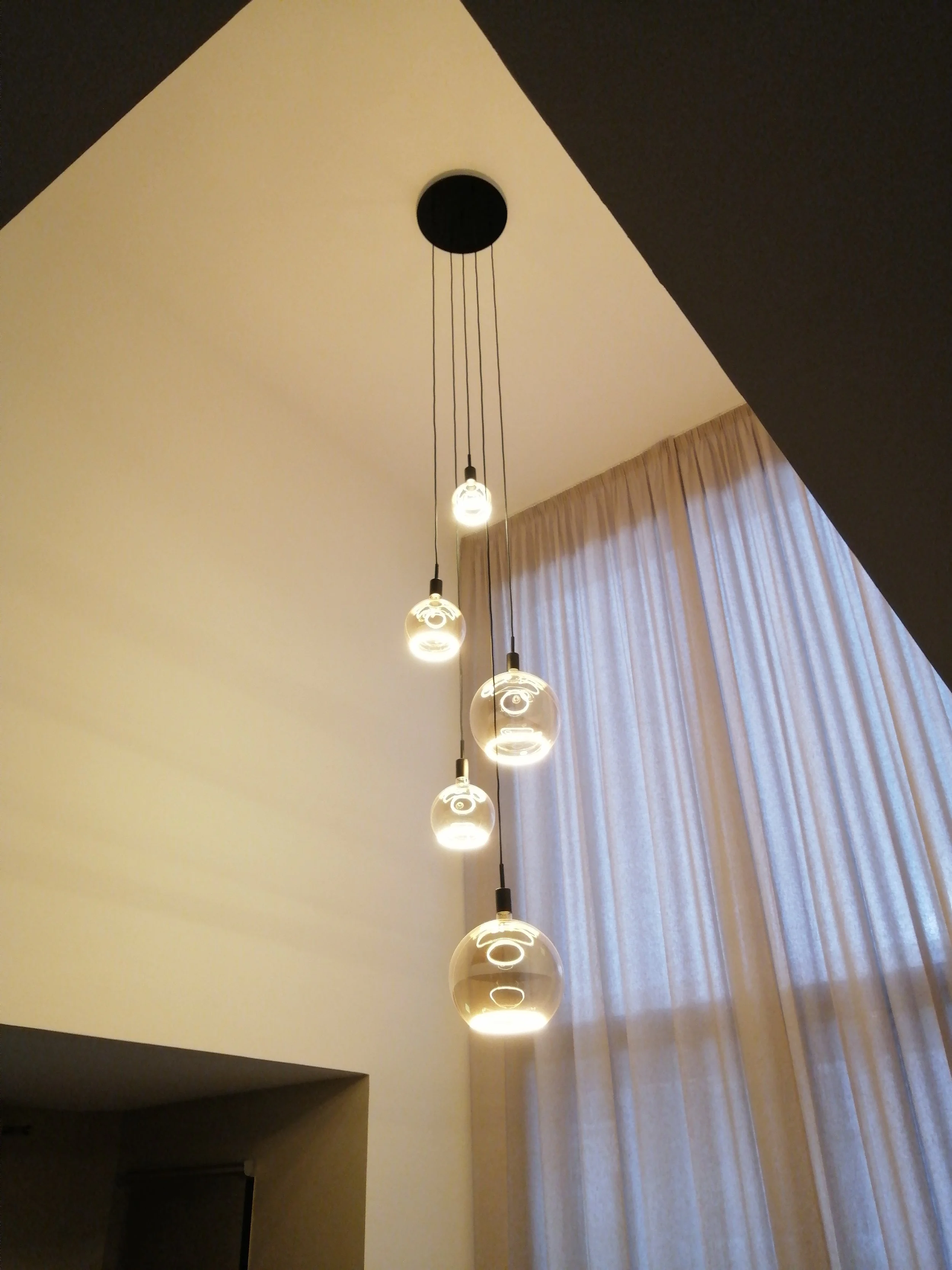 Lustre moderne avec plusieurs ampoules suspendues devant un rideau blanc.