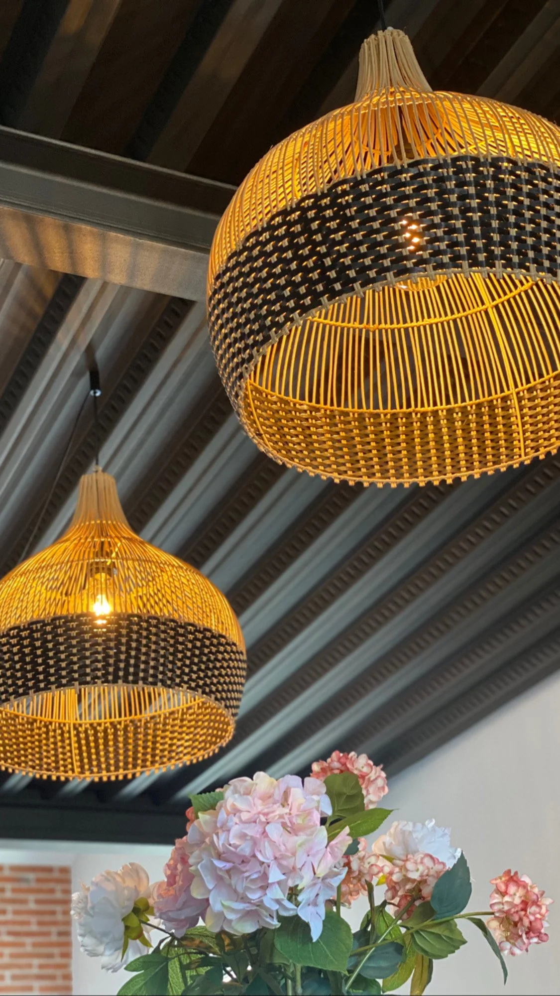 Deux suspensions en rotin lumineuses et un bouquet de fleurs roses et blanches en dessous.