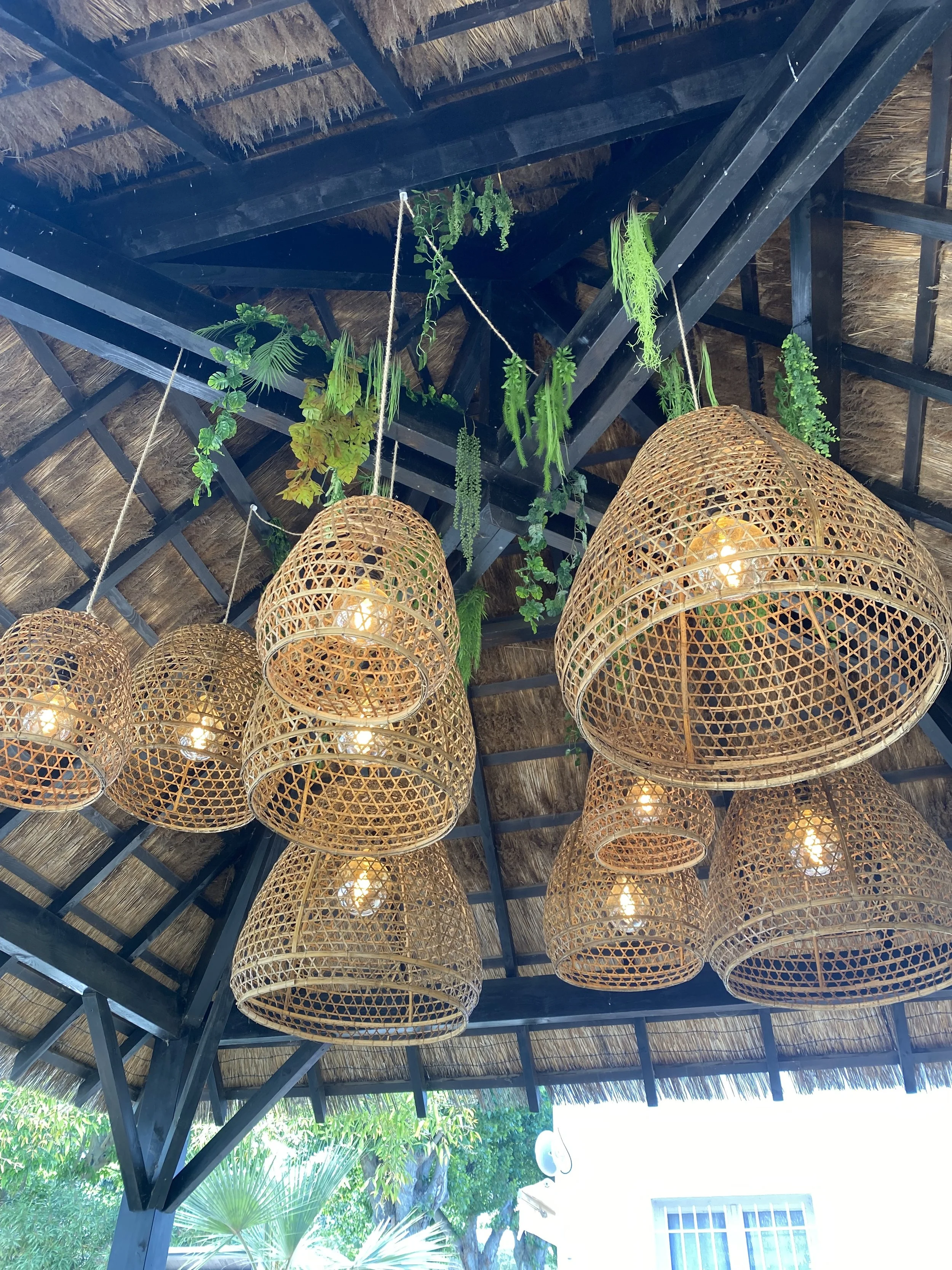 Lampes suspendues en osier sous un toit en paille et bois avec des plantes vertes décoratives.
