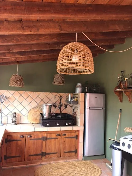 Cuisine rustique avec plafonds en bois, lampes suspendues en osier, réfrigérateur en acier inoxydable, meubles en bois, plan de travail carrelé, et accessoires de cuisine.