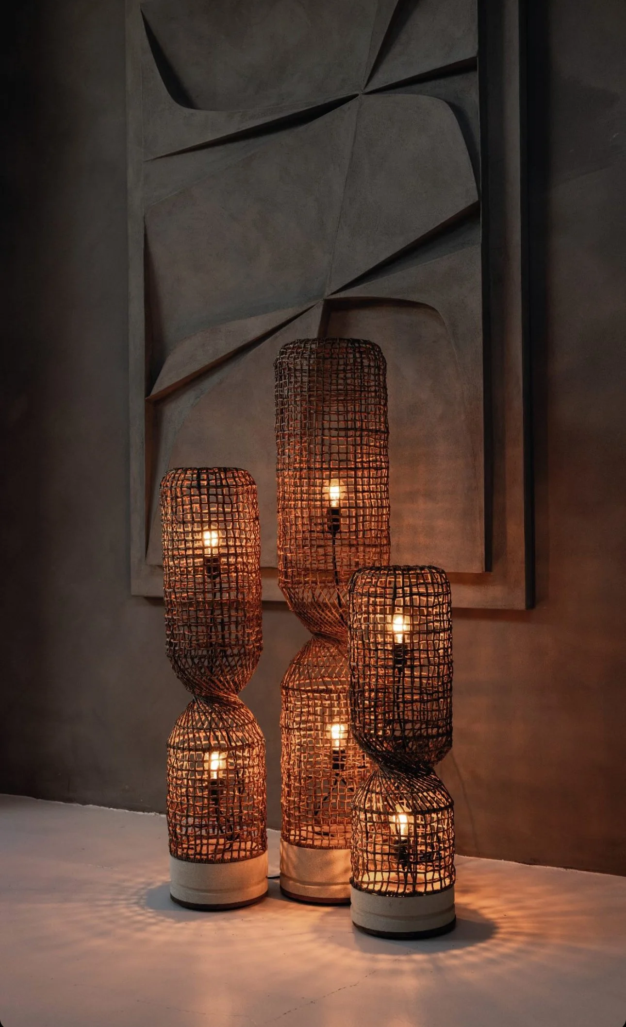 Lampes sculpturales en fibre d'abaca allumées, disposées devant un mur texturé 