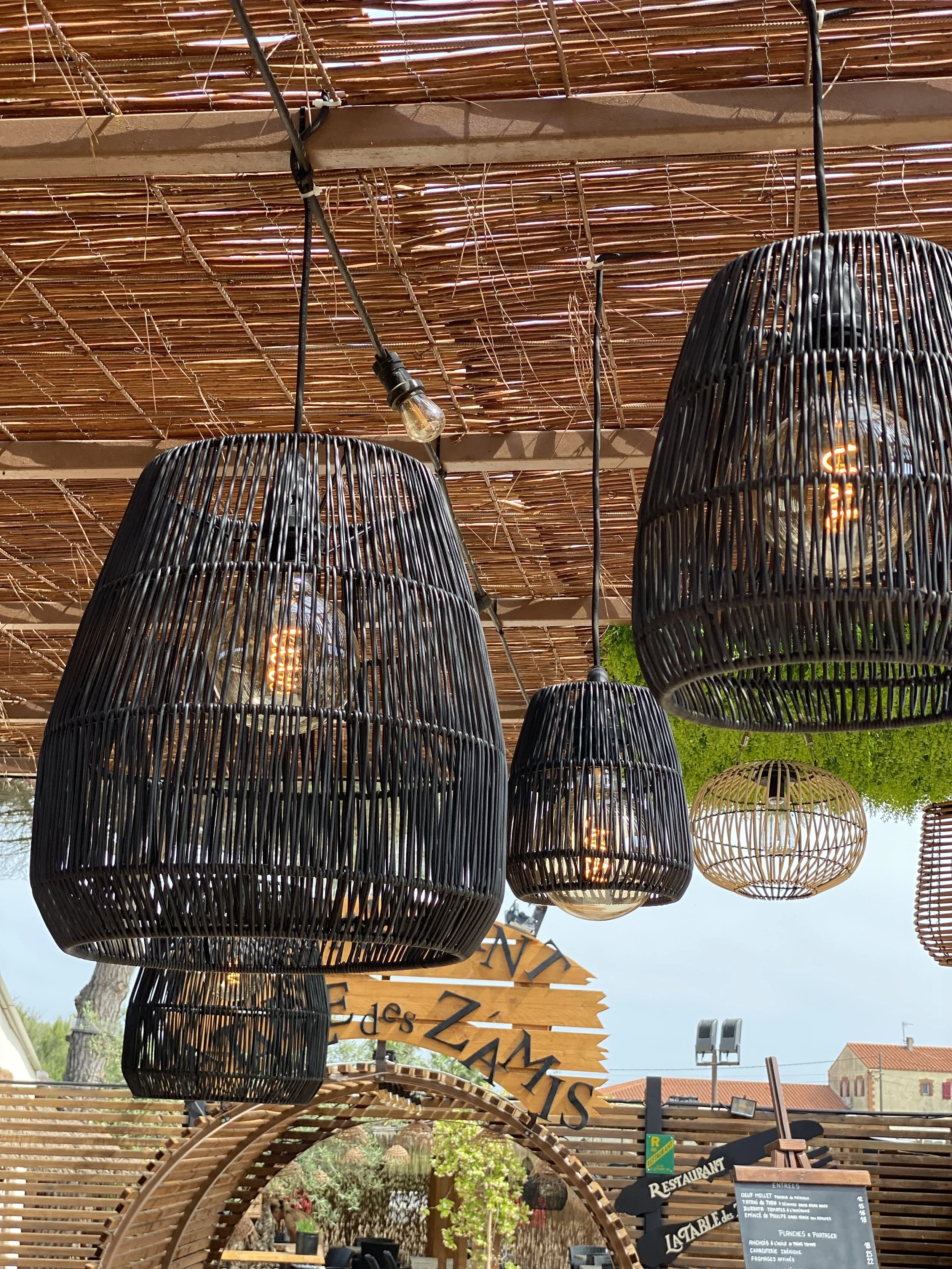 Suspensions en osier sous une pergola en bambou, éclairées avec des ampoules Edison, dans un espace extérieur décoratif.
