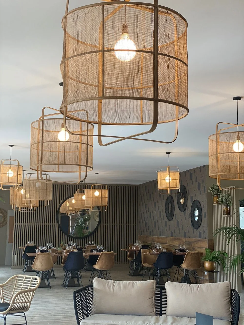 Intérieur d'un restaurant moderne avec des lustres en osier, des tables et chaises élégantes, et des miroirs décoratifs sur les murs.