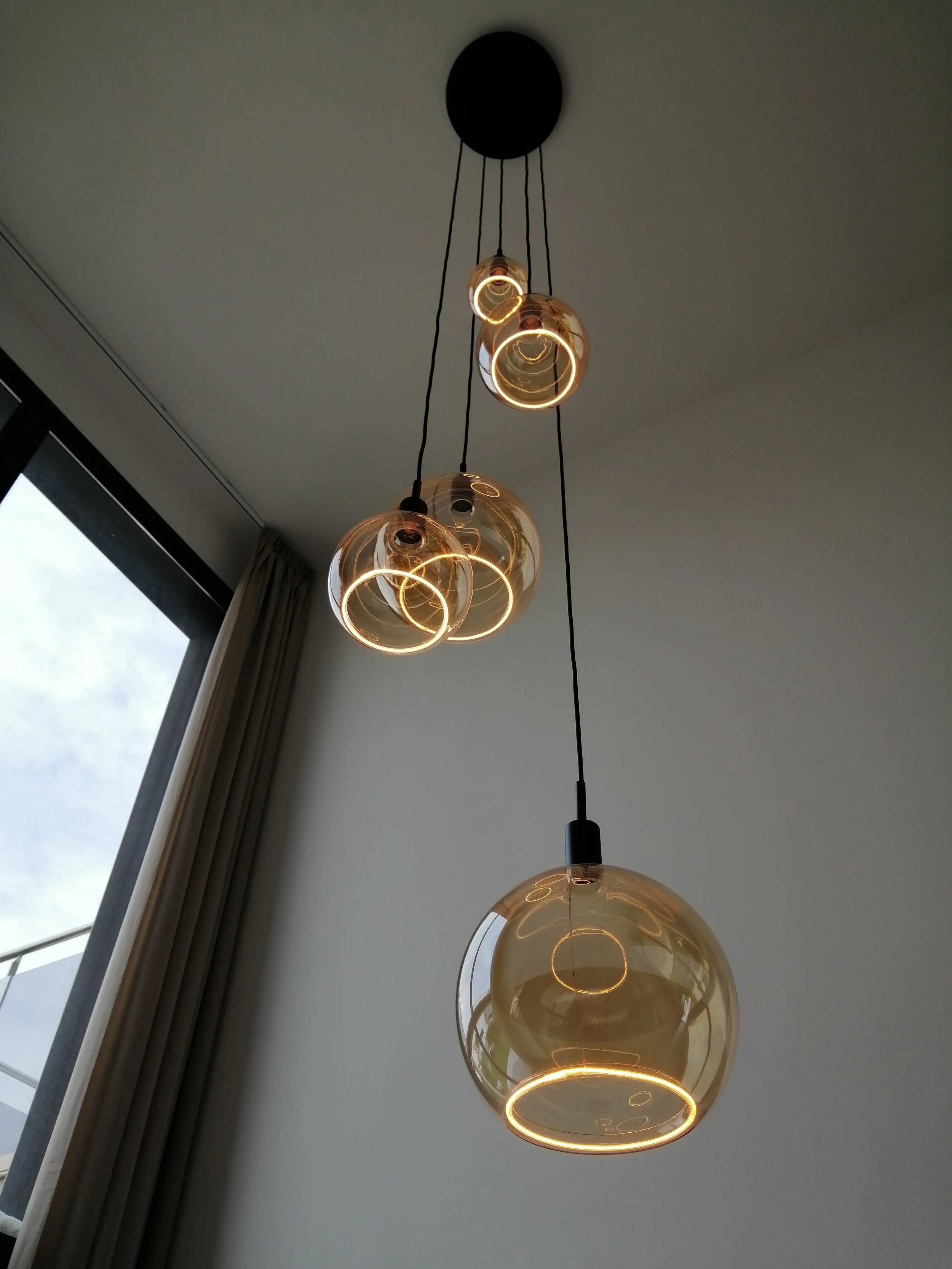 Suspension de lampes en verre avec ampoules allumées, fixée au plafond, dans une pièce moderne.