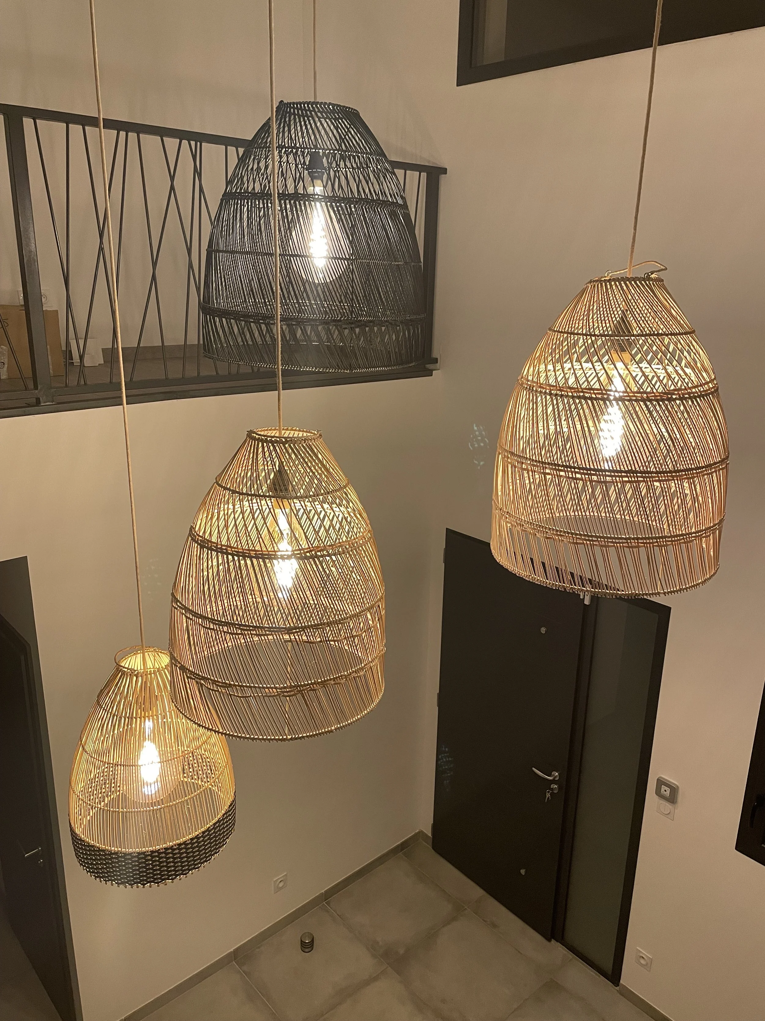 Lampes suspendues en osier dans une entrée moderne, avec sols en carrelage et porte noire.