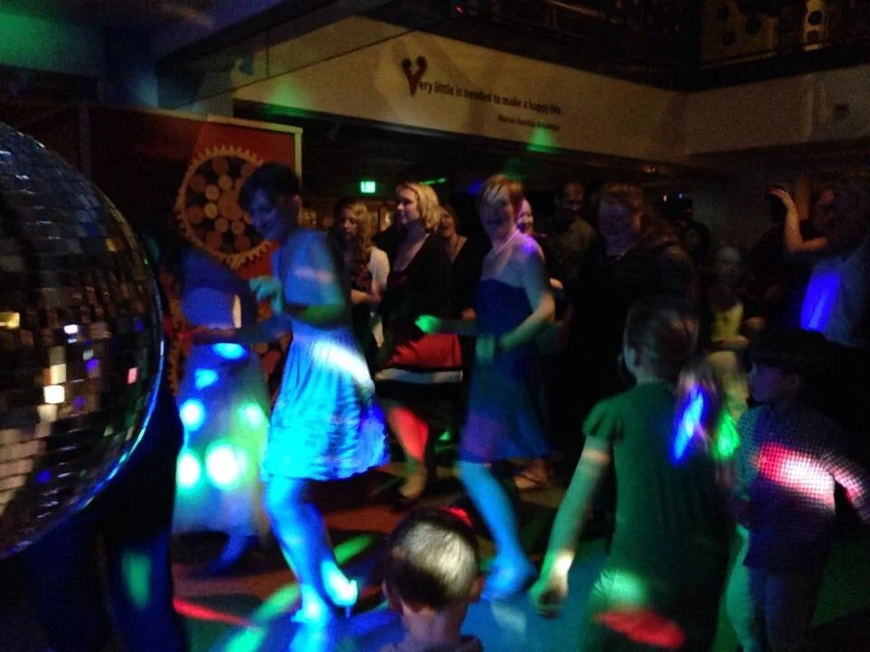 People dancing under colorful lights and a disco ball at a party.