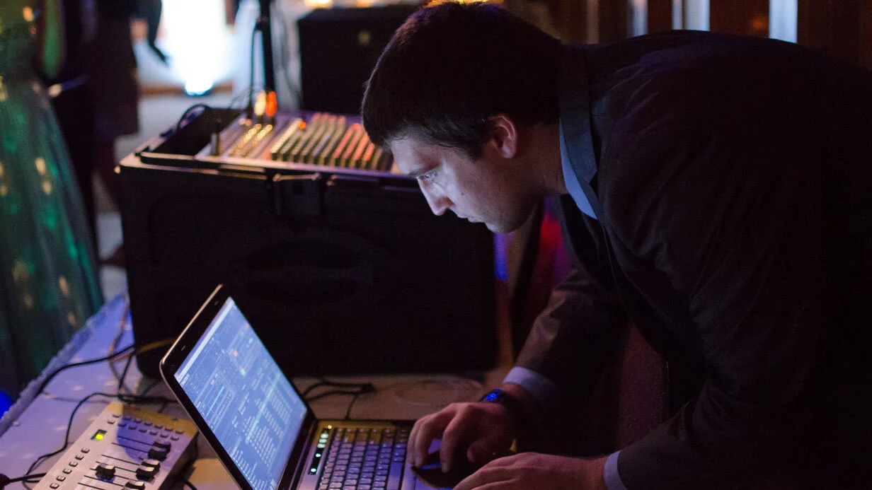 Man operating DJ equipment and laptop at an event, focusing on sound mixing.