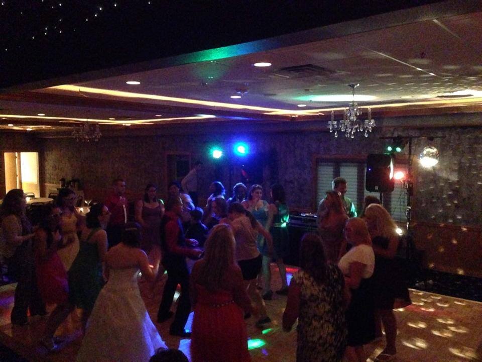 A group of people dancing at an indoor party with colorful lights, a DJ booth, and a decorated ceiling.
