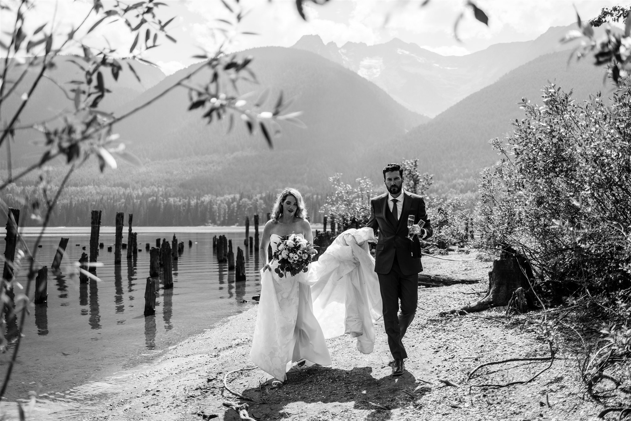 Bride and groom walking on a beach with a bottle of champagne.