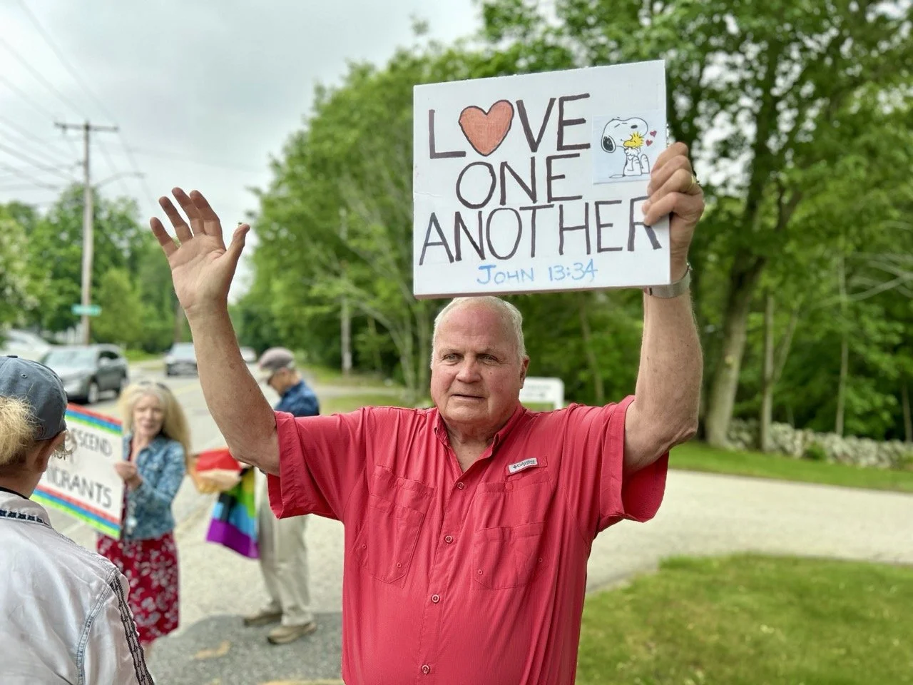 people stand out with signs and flags that say "together we rise" and "god loves all"