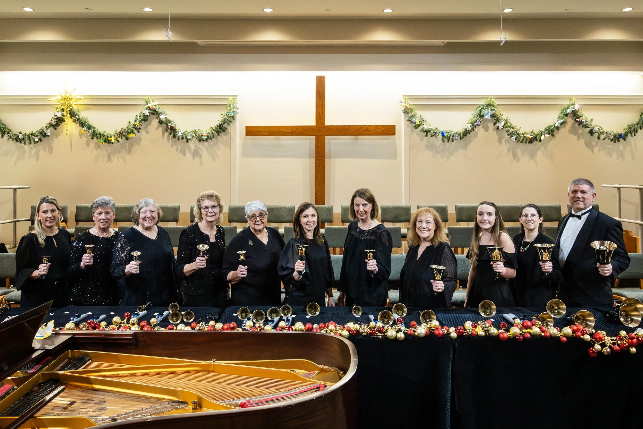 A group of performers holding a bell in one hand and smiling at the camera.